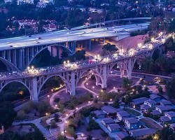 Nighttime cityscape with illuminated arches and bridges over a landscaped area.