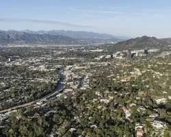 Aerial view of a city with mountains in the background, showing urban and suburban areas with roads and greenery.
