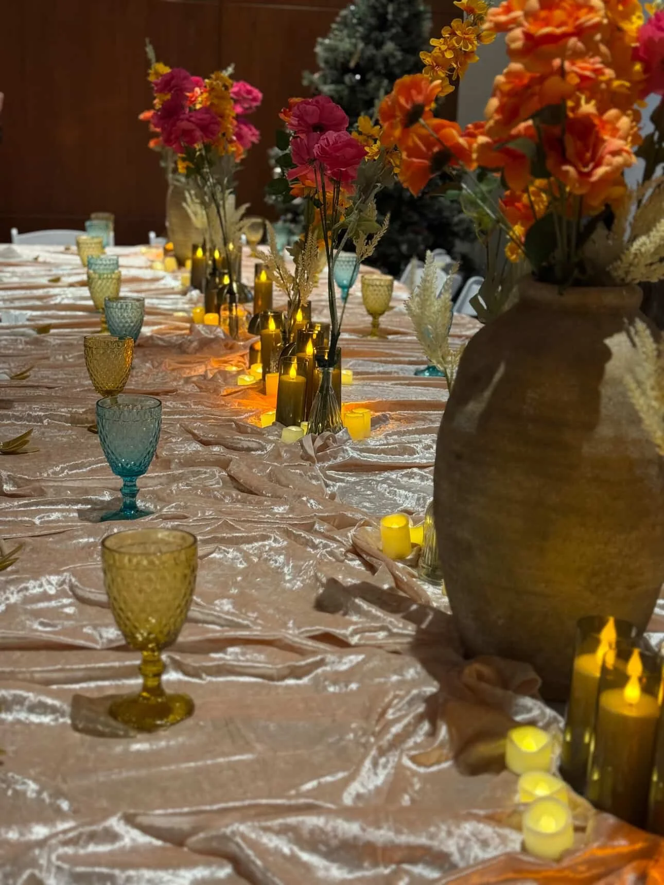 A decorated dining table with flower vases, colorful glassware, and candlelight candles.