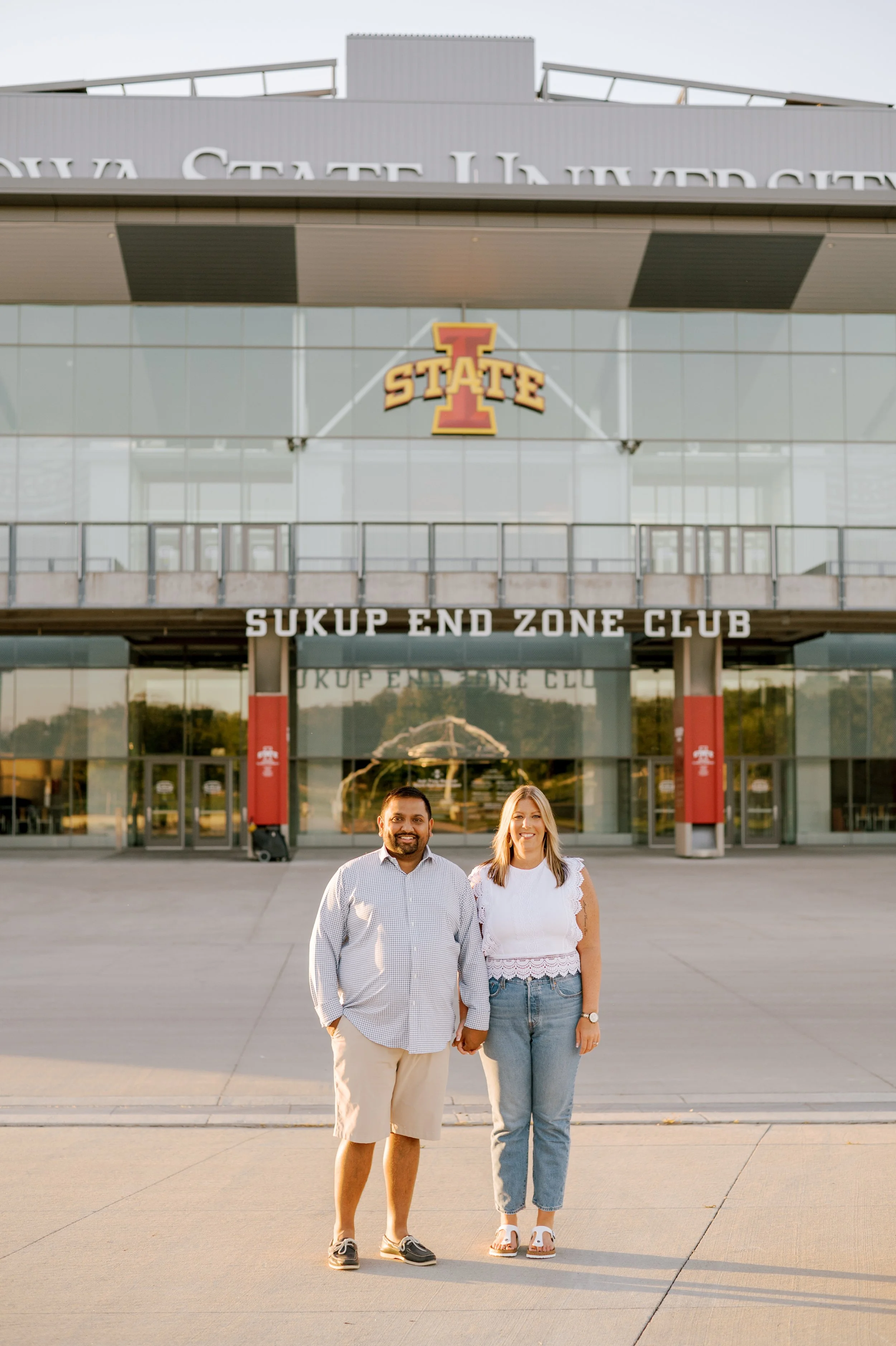 A man and a woman standing in front of the Sukup End Zone Club at Iowa State University, holding hands and smiling.
