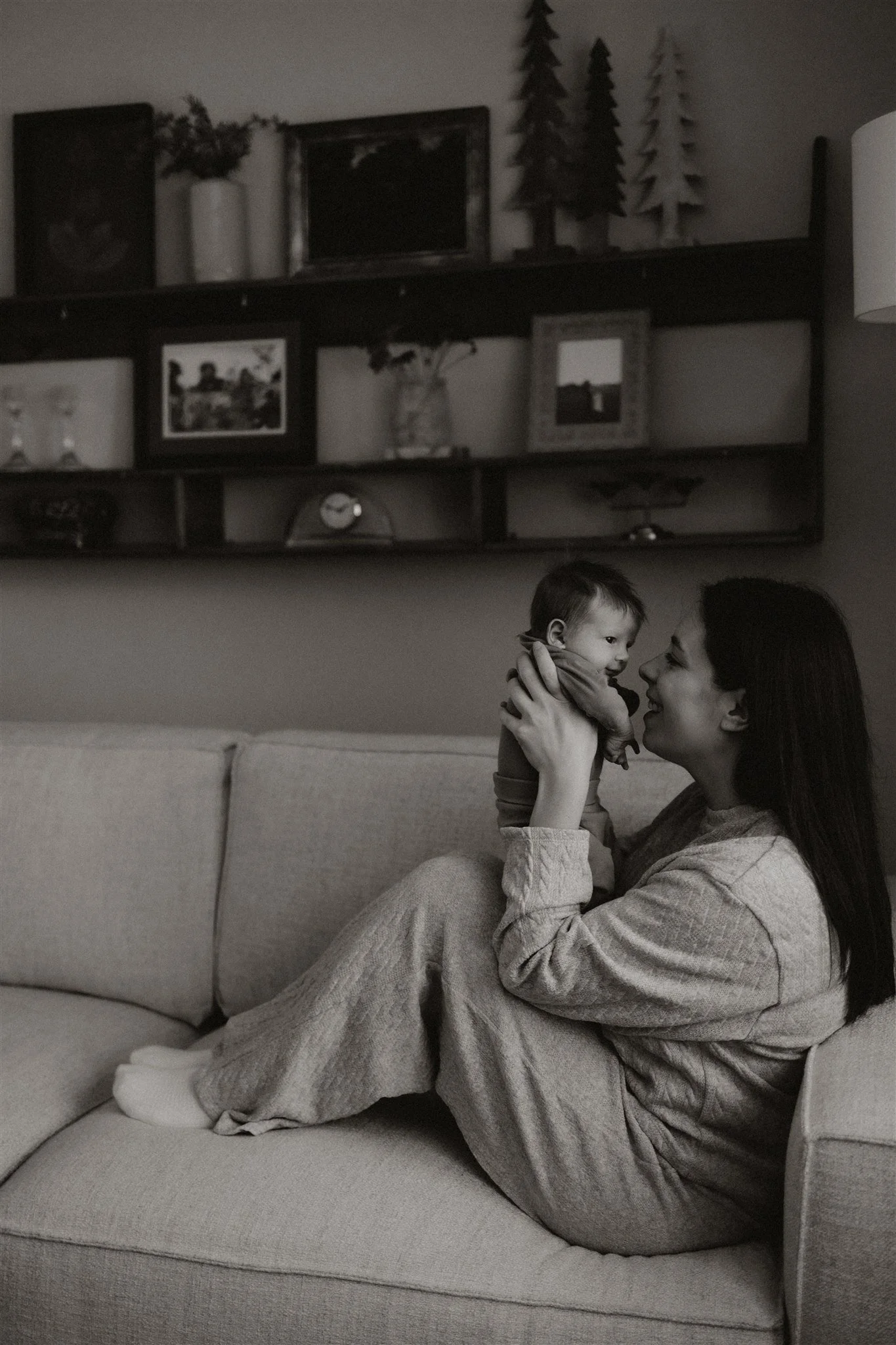 A woman holding a baby on a beige sofa in a living room.