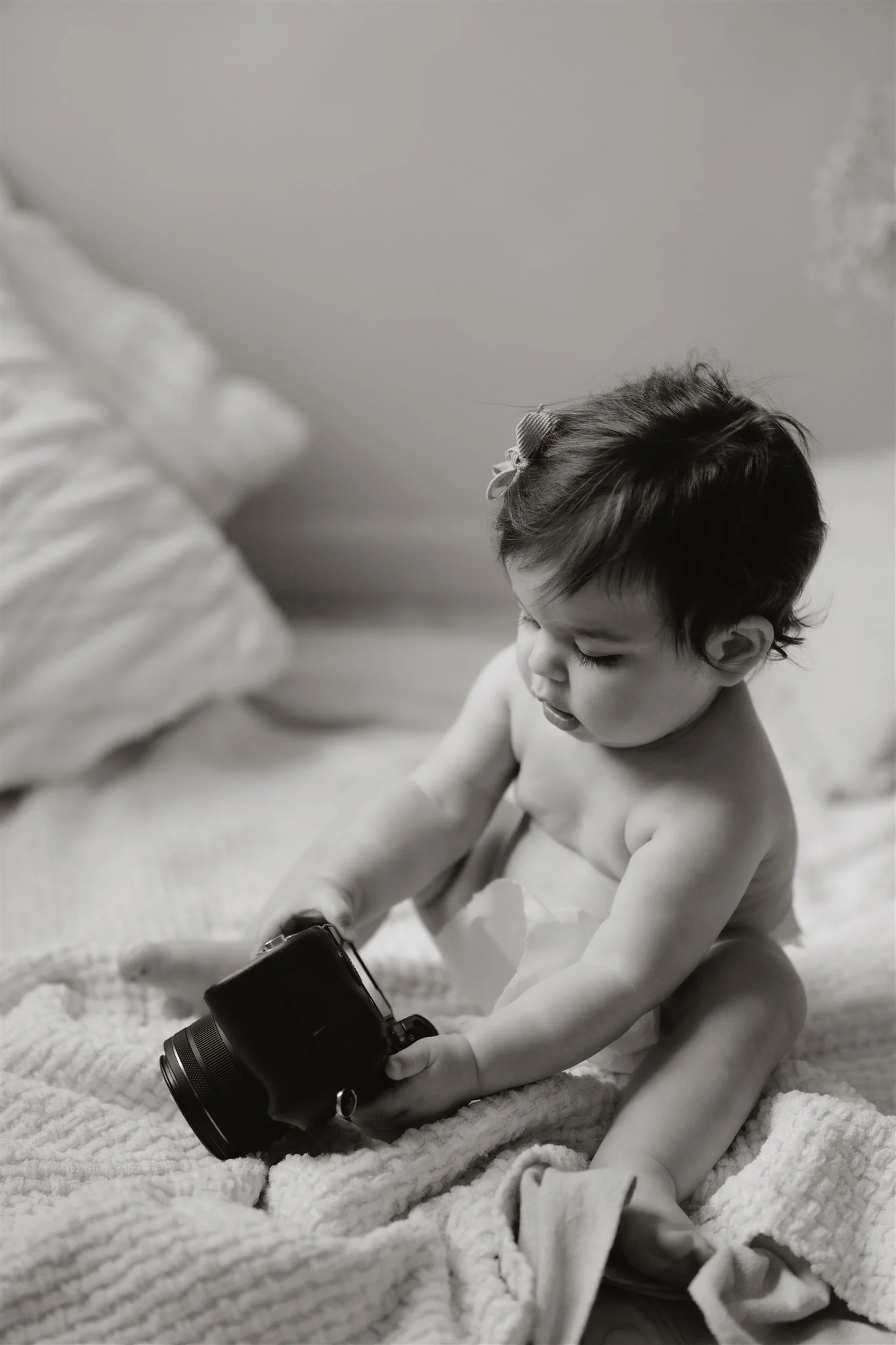 A young child, sitting on a cozy blanket, looking at a camera in their hands.