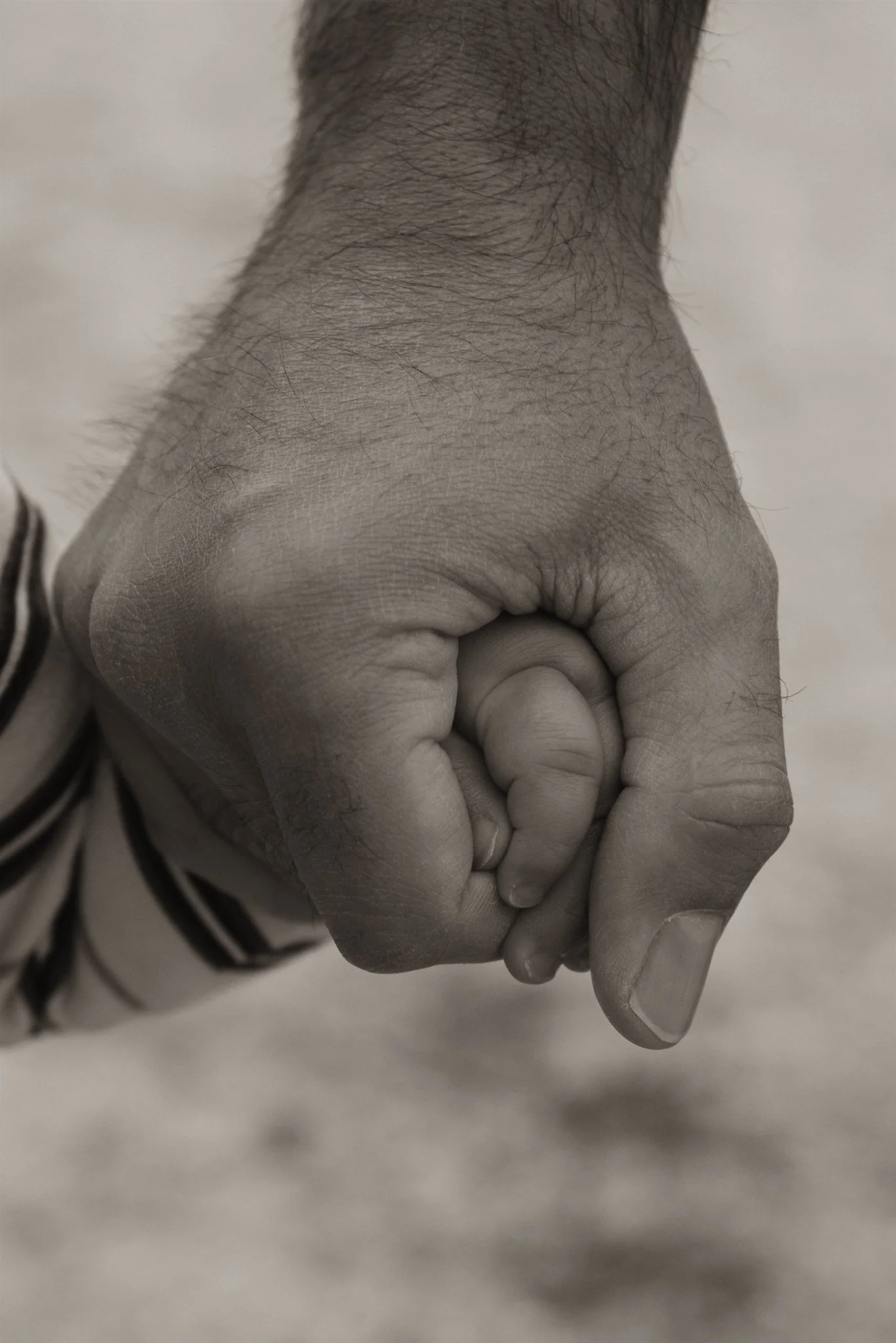 A close-up of an adult's hand holding a small child's hand, with both hands forming a circle, in black and white.