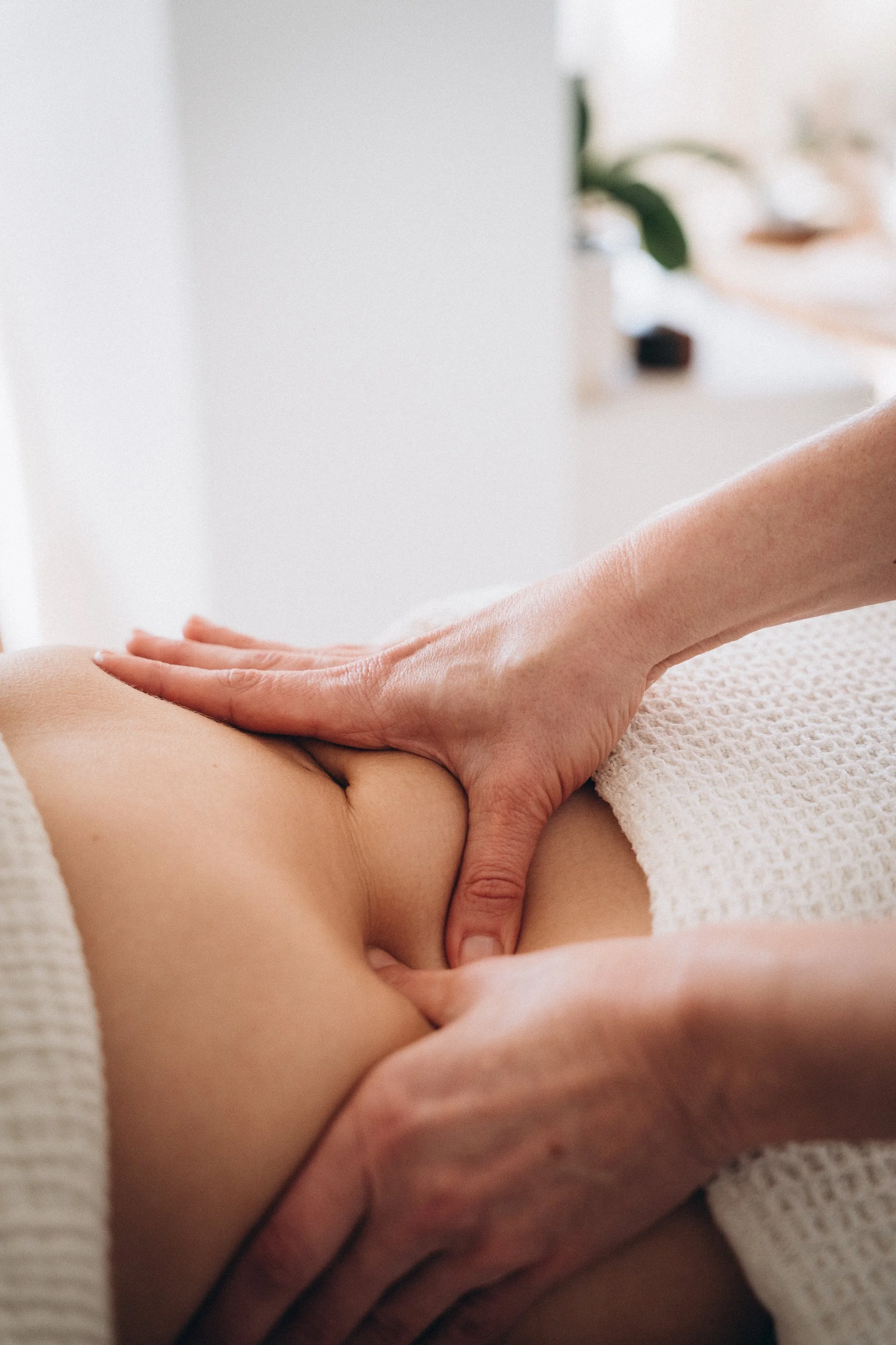 Une personne reçoit un massage de dos dans un cadre de spa ou de massage, avec une main en train de masser la partie inférieure du dos, entourée d'une serviette blanche.