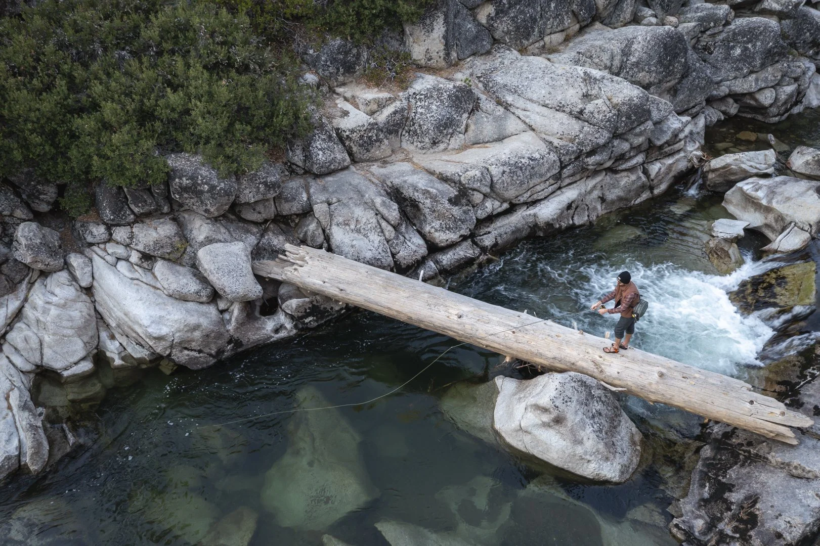 Man fly fishing from a log in the Northern Sierra, California during a Royal Robbins assignment, photographed by Fieldborn Creative.