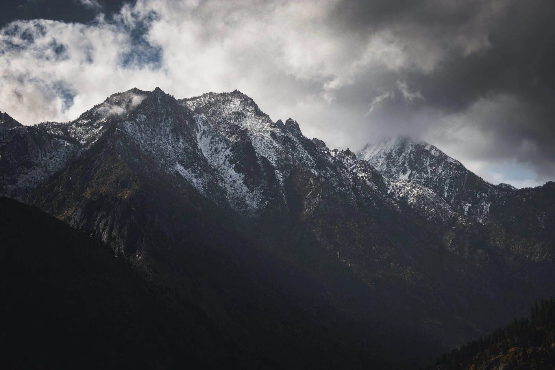 Mountain range with snow-capped peaks under cloudy sky.
