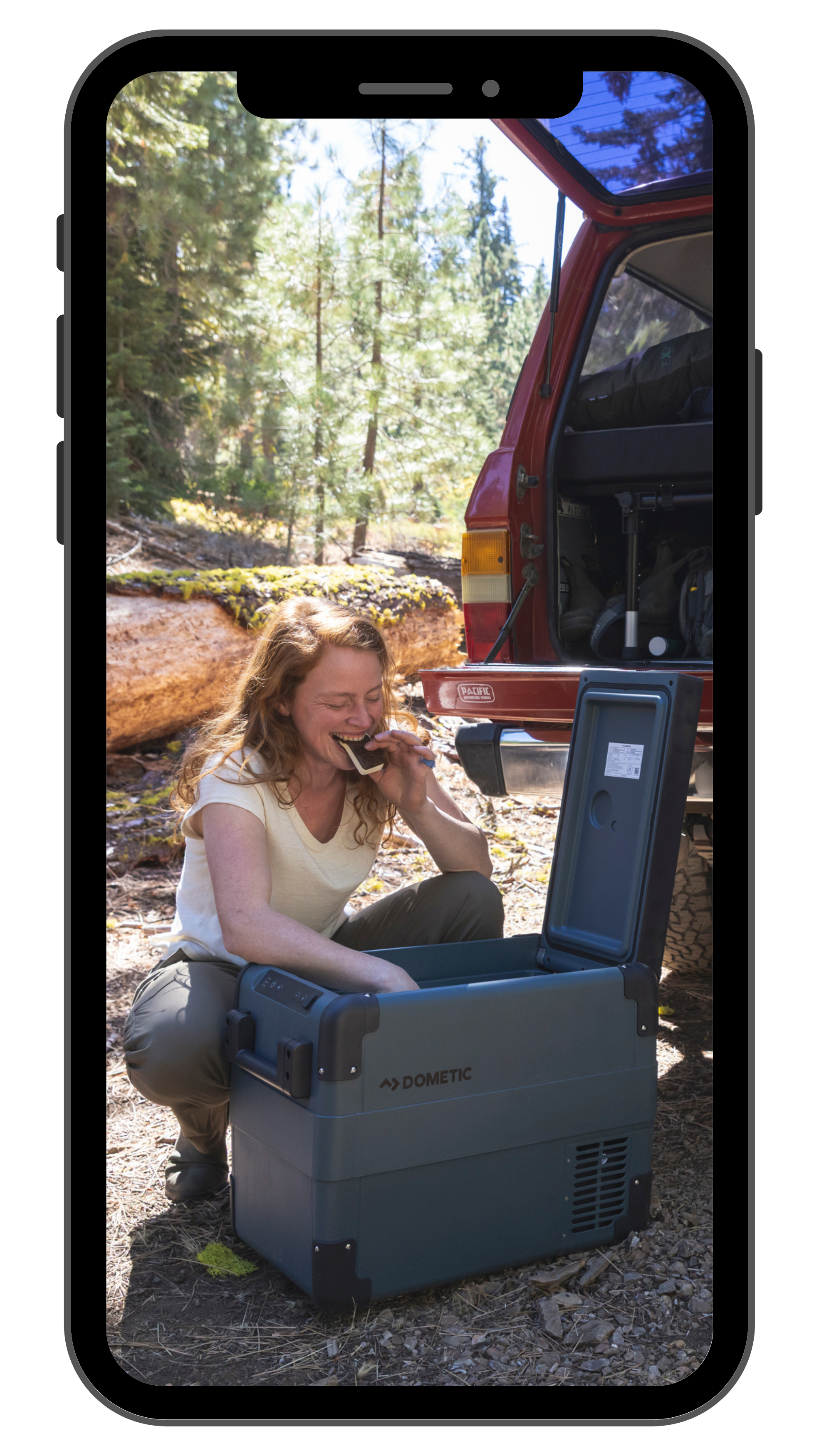 Woman using a Dometic cooler and eating an ice cream sandwich near a tailgate in the woods of Northern California, photographed by Fieldborn Creative.