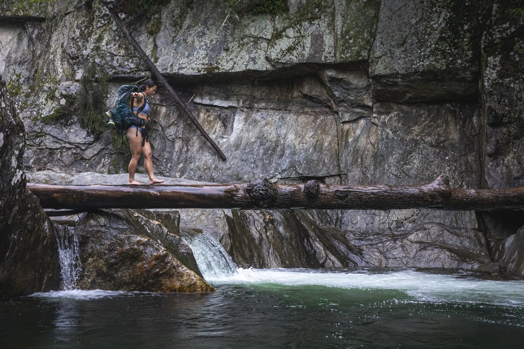 Woman crossing a wet log near a swimming hole along the Long Trail in Vermont during an Osprey assignment, photographed by Fieldborn Creative.