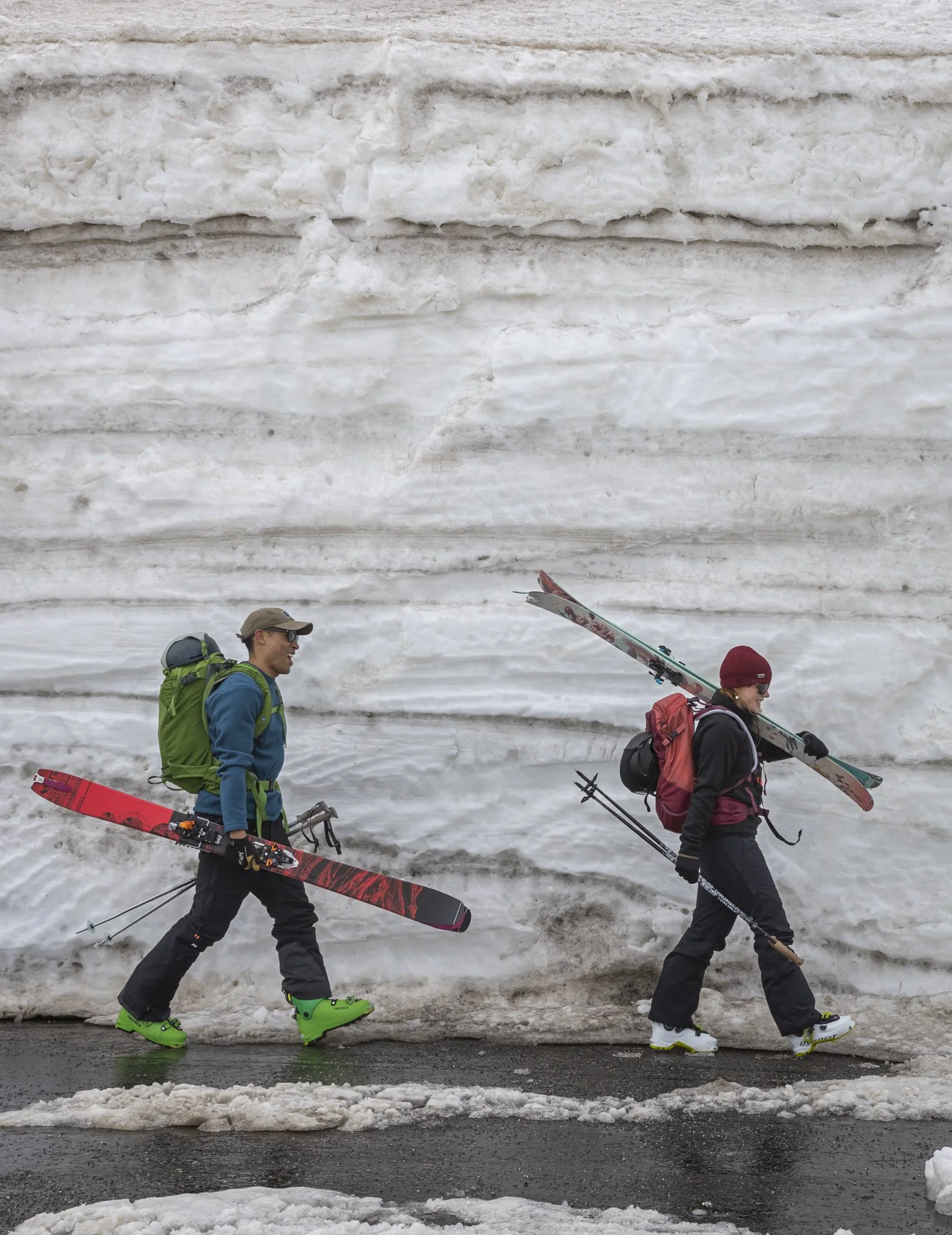 Man and woman carrying skis in front of a snow-covered wall near Donner Summit, Northern California during a Royal Robbins winter assignment, photographed by Fieldborn Creative.