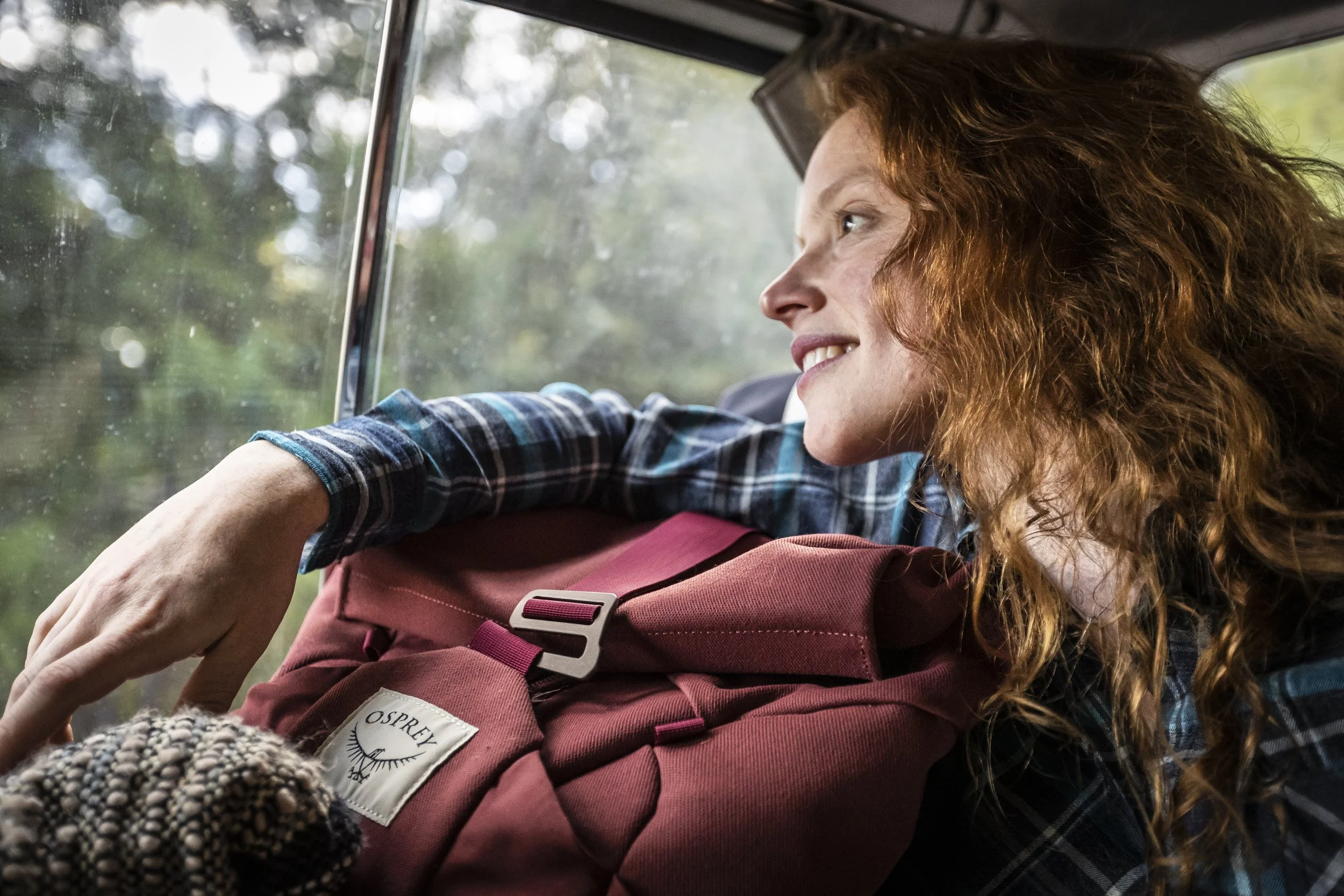 Portrait of a red-headed woman leaning on an Osprey pack in a van window with beautiful light during an Osprey lifestyle shoot in Humboldt County, photographed by Fieldborn Creative.
