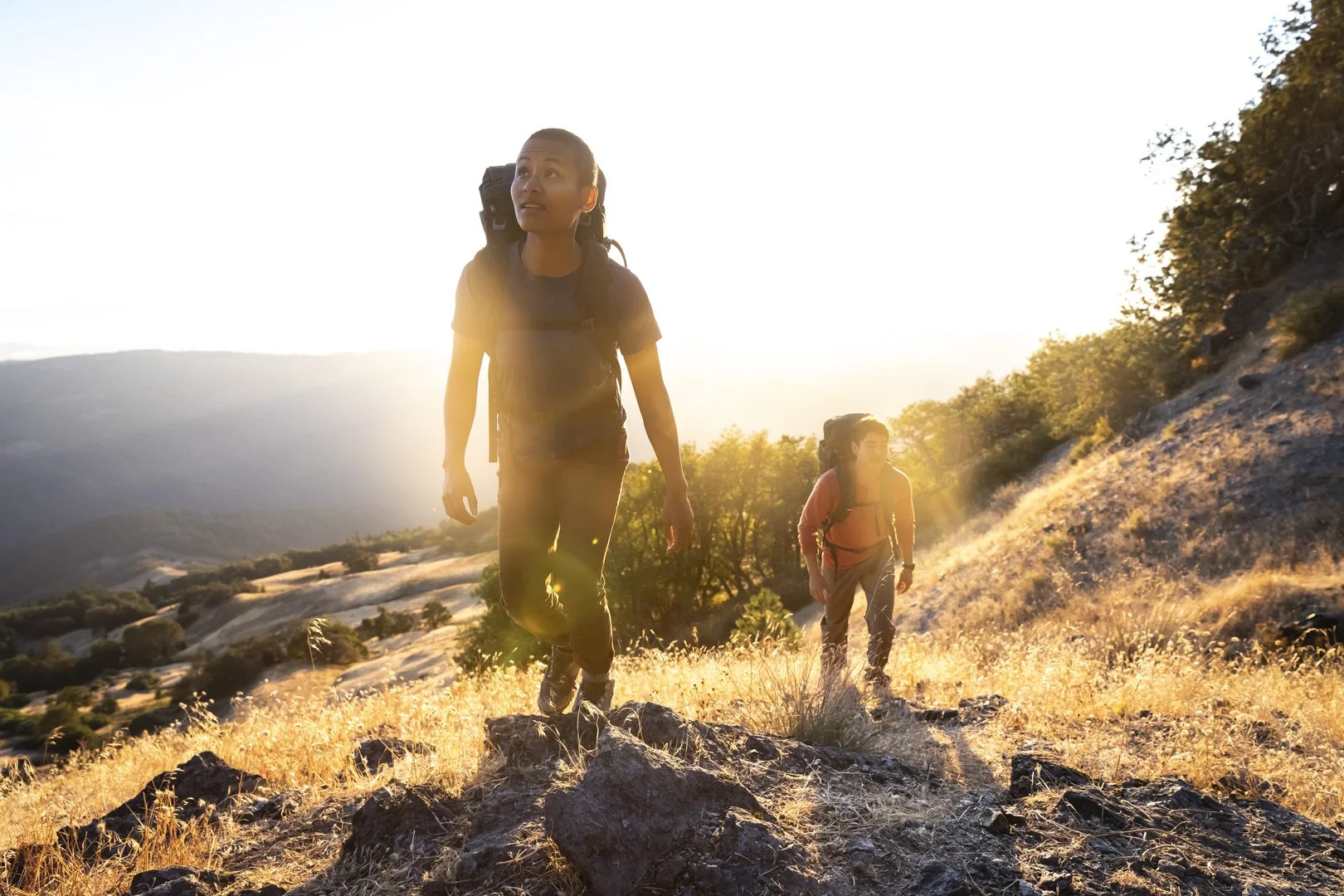 Man and woman hiking with backpacks on rocky trail at sunset, backlit by sun in Northern California, photographed by Fieldborn Creative