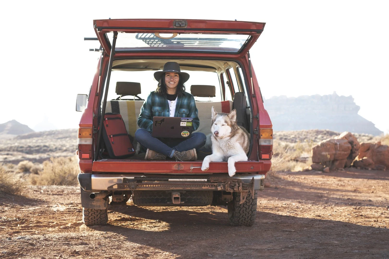 Woman with a laptop sitting in the back of a classic Land Cruiser with a dog in the Utah desert, photographed during an Osprey assignment by Fieldborn Creative.