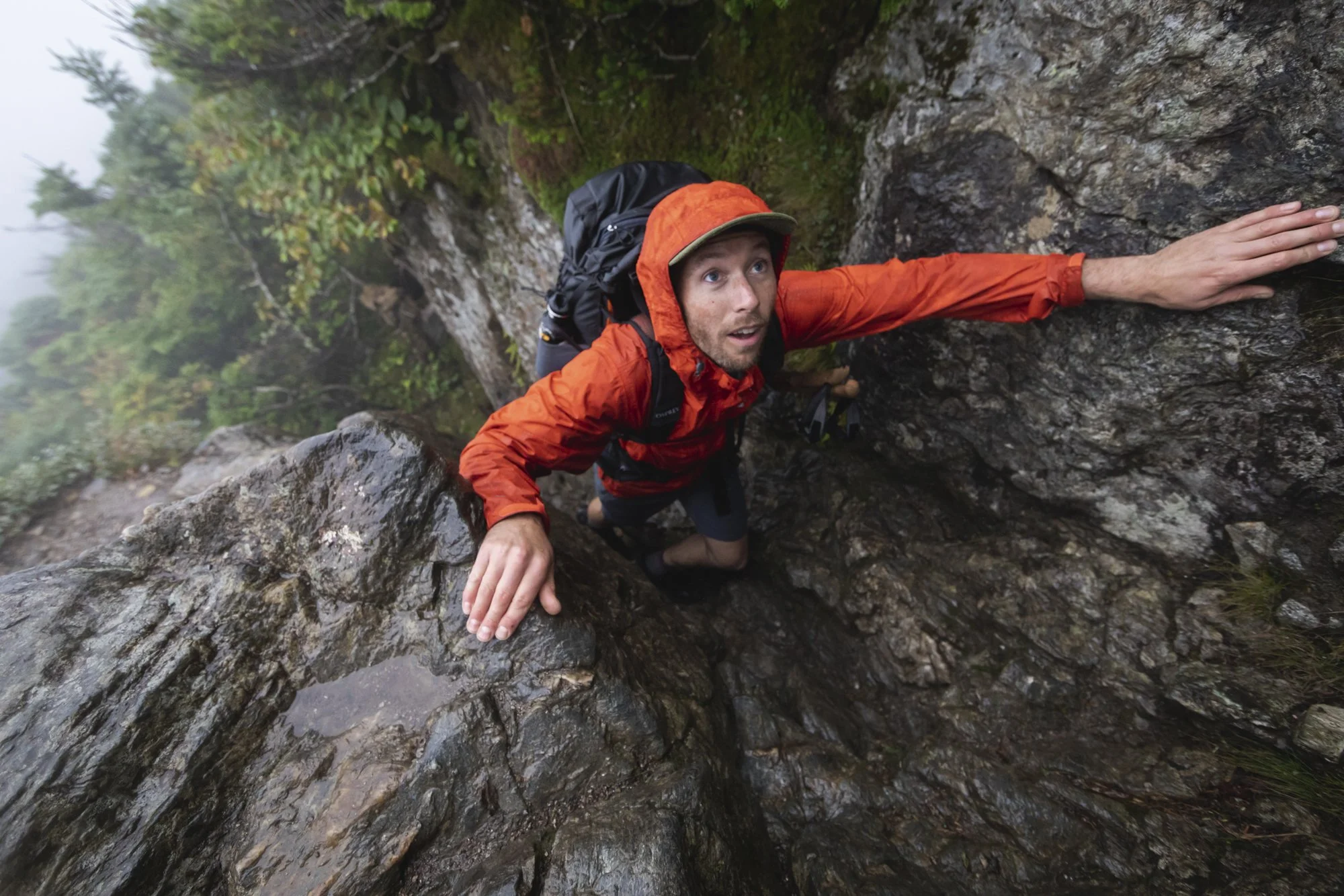 Man backpacking in Vermont, scrambling up a rock in the rain during an Osprey shoot, photographed by Fieldborn Creative.