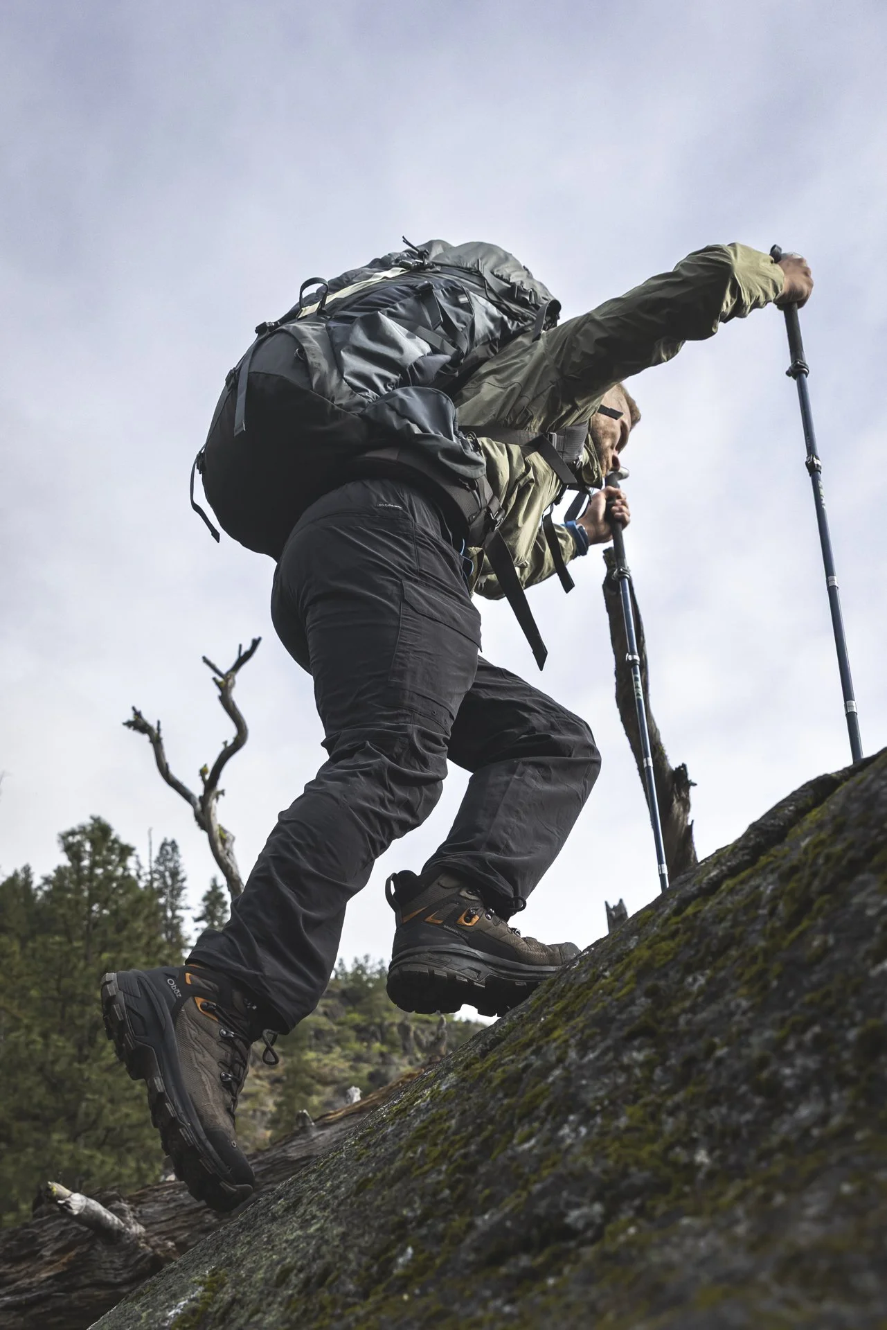 A hiker climbing a rocky incline with hiking poles, wearing outdoor gear and carrying a backpack.