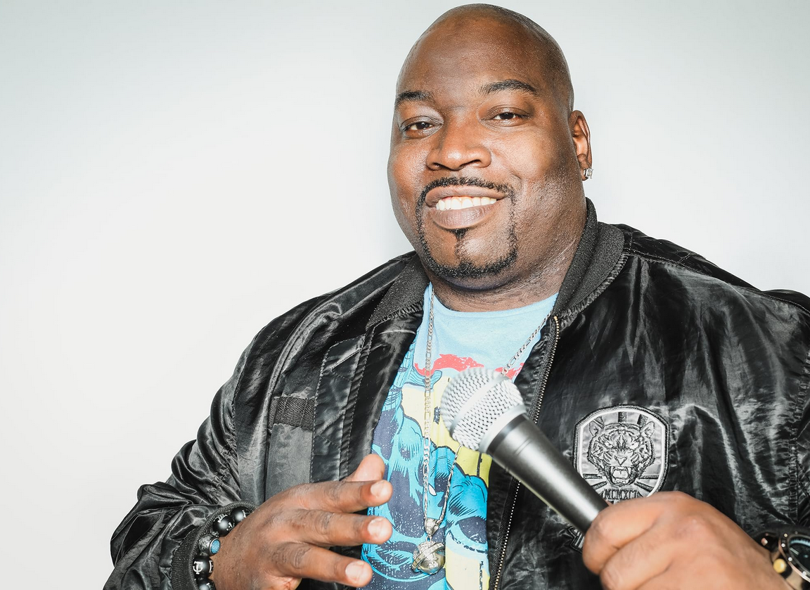 Actor, Former Pro-Wrestler, and Comedian Jay Washington, now represented by ATFP, is smiling in a black leather jacket and holding a microphone in front on a white background.