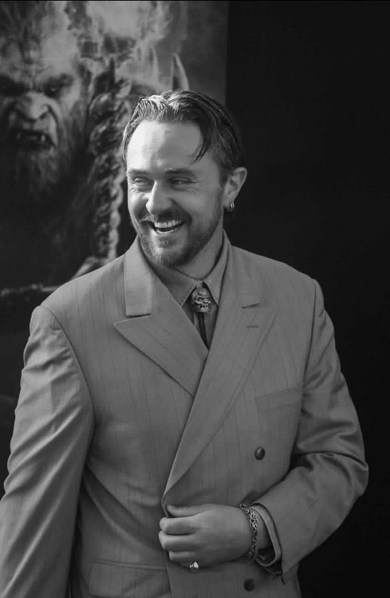 Actor Sam C Wilson smiling and laughing in a striped double breasted suit jacket and Trap Jaw bolo tie at a Masters of the Universe(2026) premiere.
