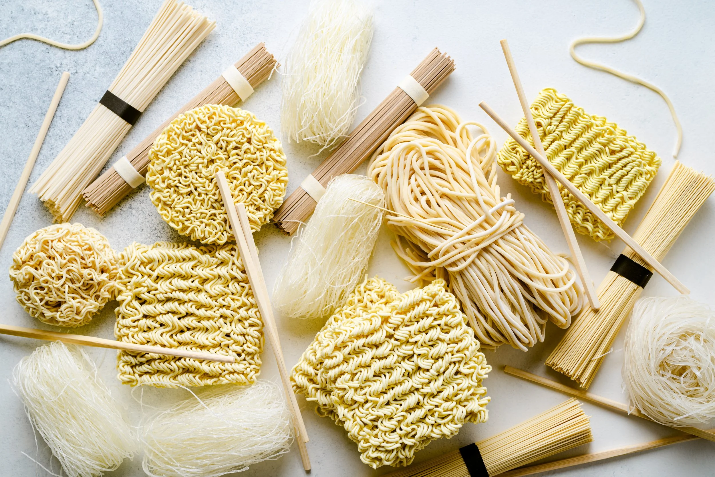 Assorted uncooked Asian noodles, including thin vermicelli, straight bundles, and curly noodle blocks.