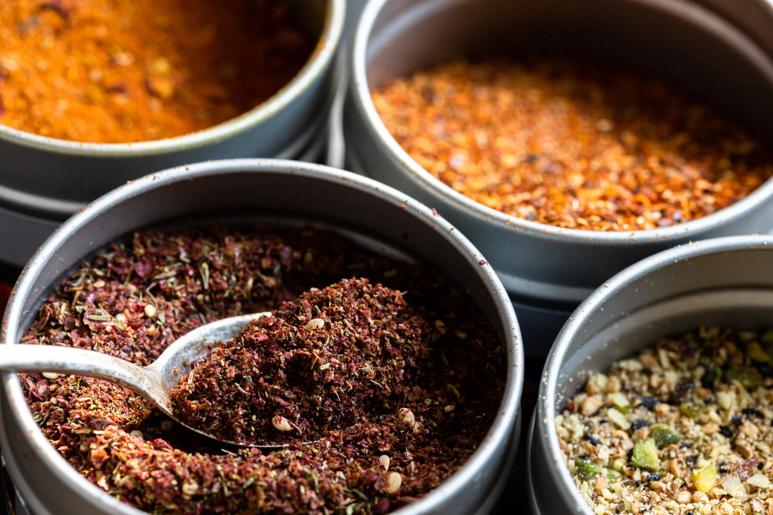 Assorted ground spices and herb blends in metal bowls, with a spoon holding a reddish spice mixture.