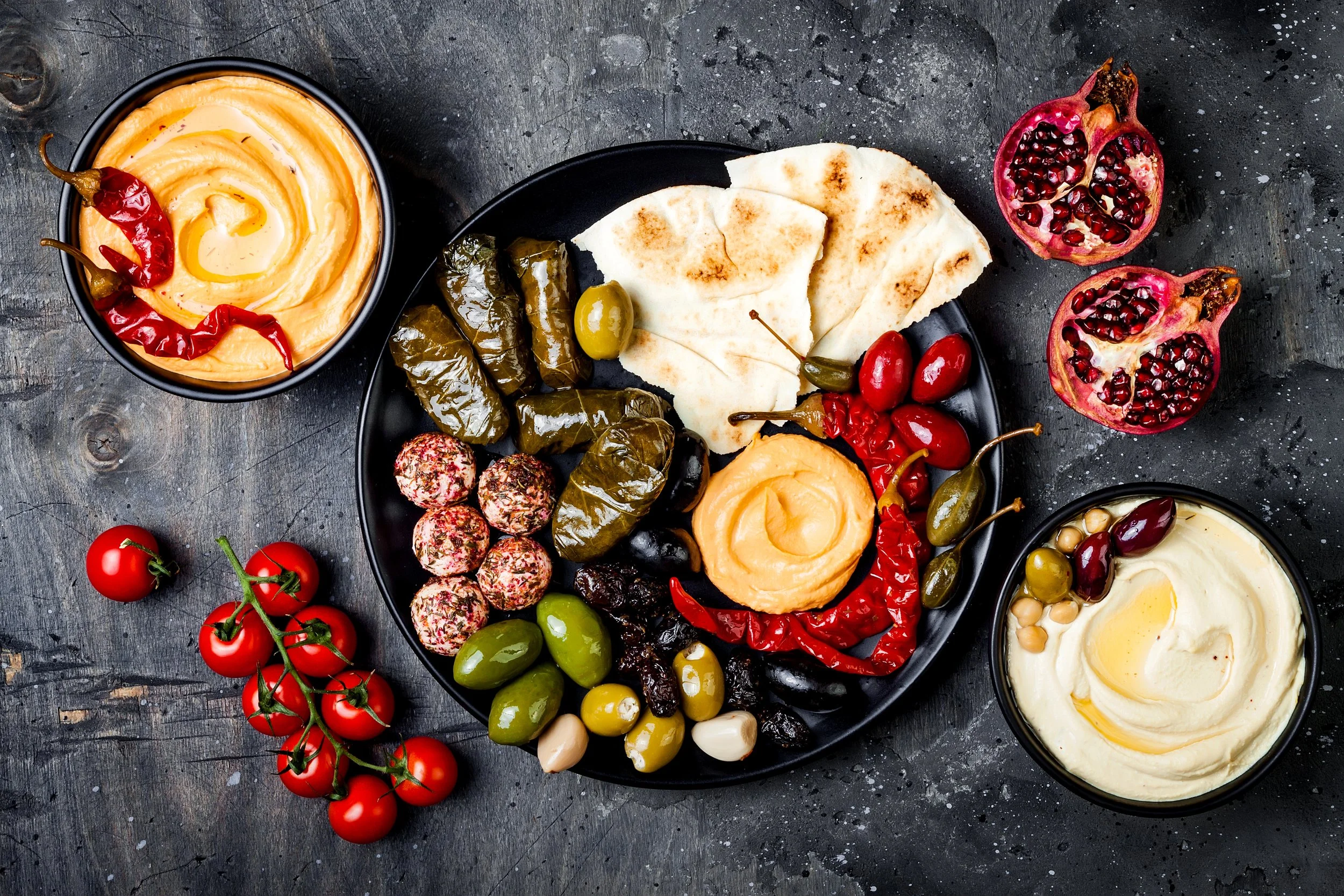 Mezze platter with pita, hummus, olives, stuffed grape leaves, and seasoned labneh balls.