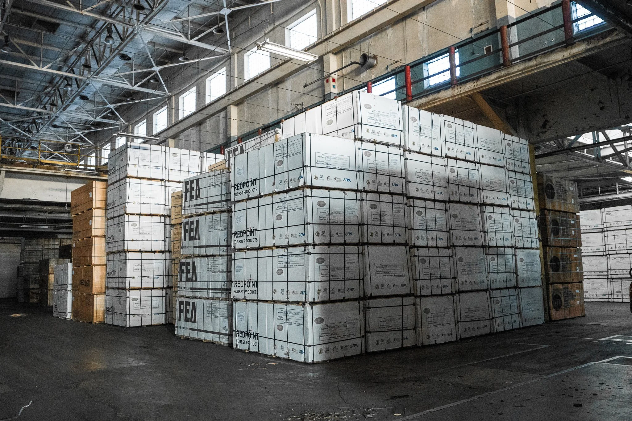Stacks of boxes in a warehouse with high ceiling and industrial lighting.