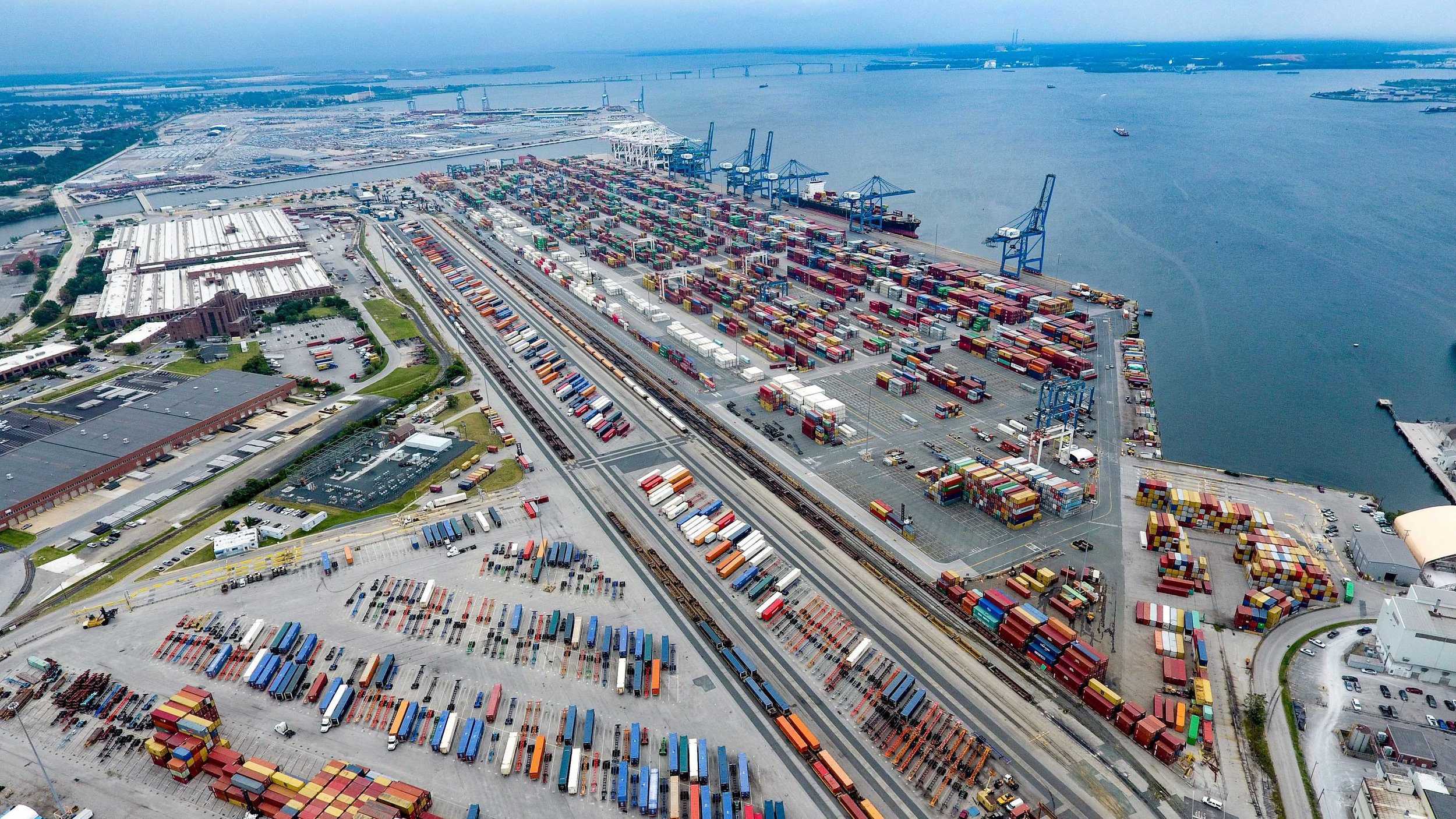 Aerial view of a busy port with numerous containers, cranes, train tracks, and shipping facilities near the water.