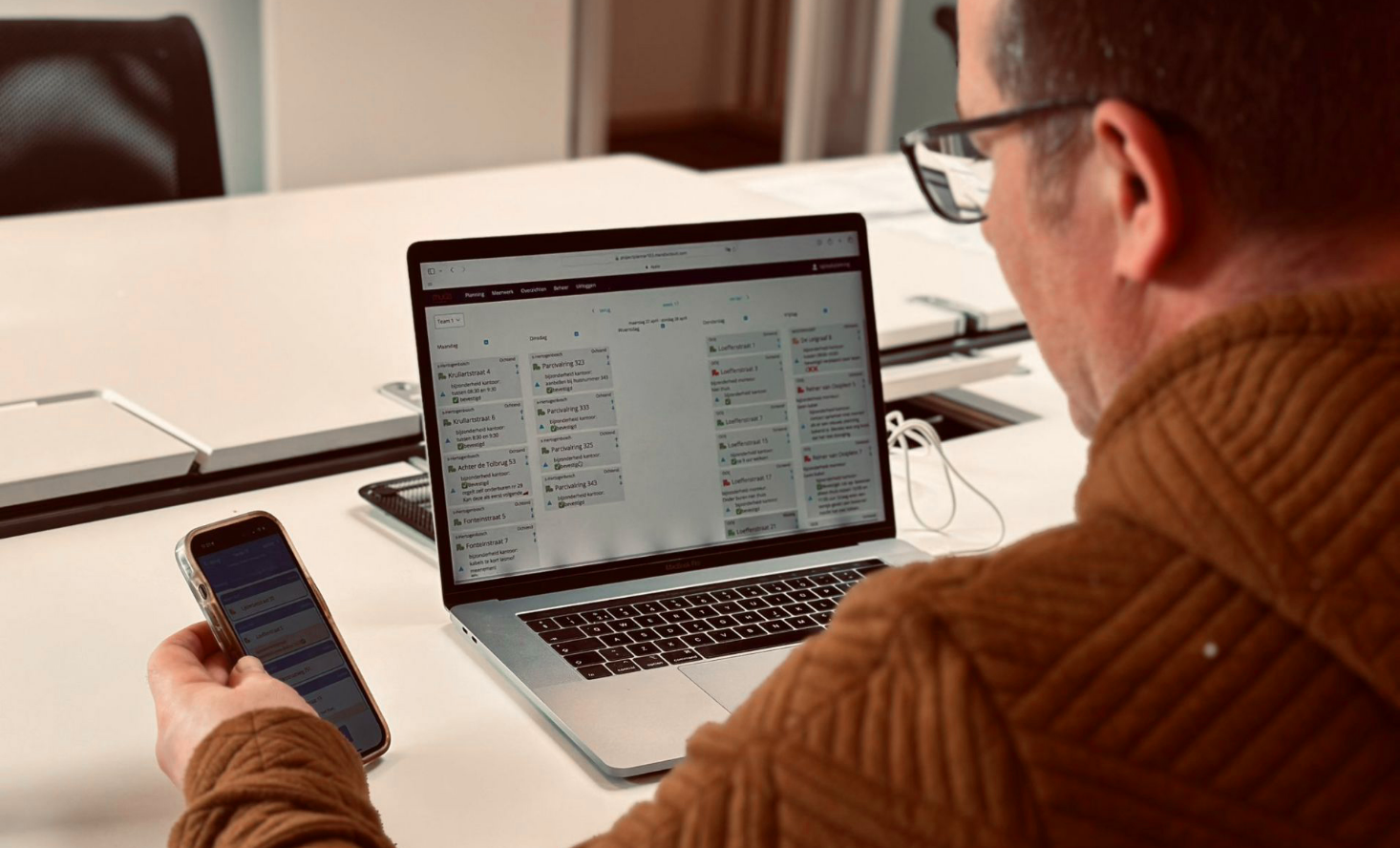 Man bekijkt een smartphone en een laptop op een tafel in een vergaderzaal, met documenten op de tafel.