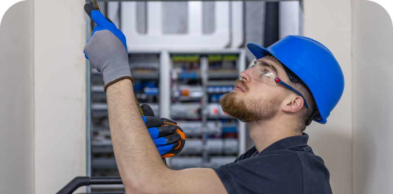Ein Elektriker von Skyber, der einen Schutzhelm und eine Schutzbrille trägt, öffnet eine kleine Box in einem Elektroschrank.