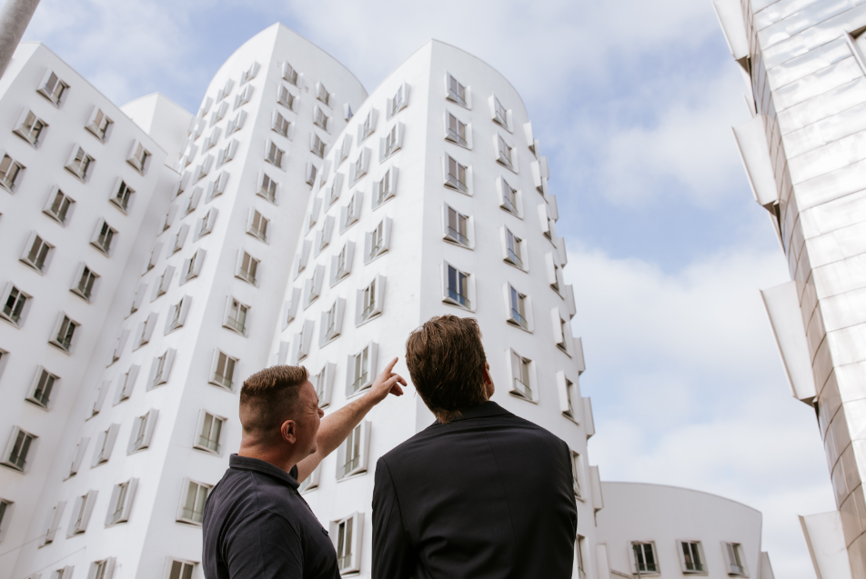 Twee mannen die naar een modern wit appartementencomplex kijken en erover discussiëren