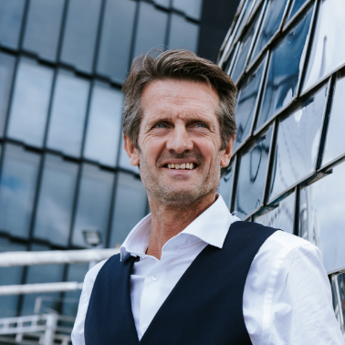 Portret van een man in zakelijke kleding buiten een modern kantorengebouw.