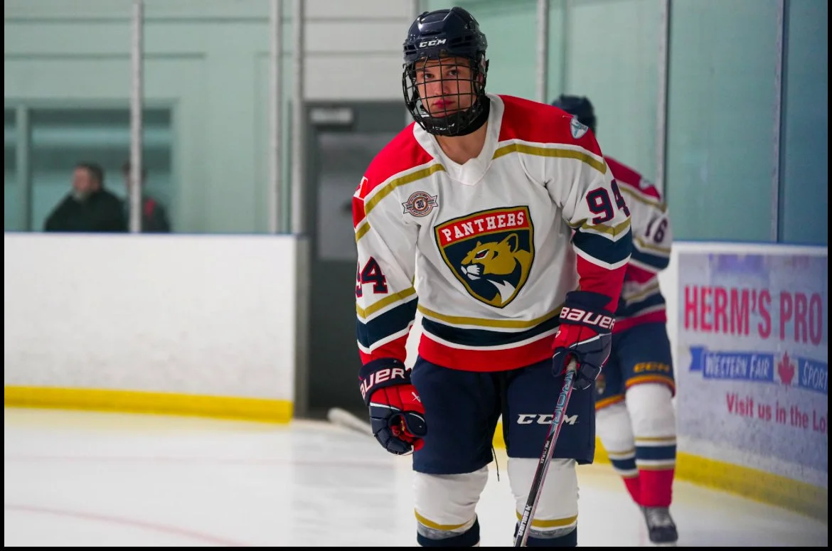 Hockey player in a white, red, and blue uniform with a panther logo, wearing a helmet and gloves, on the ice rink.