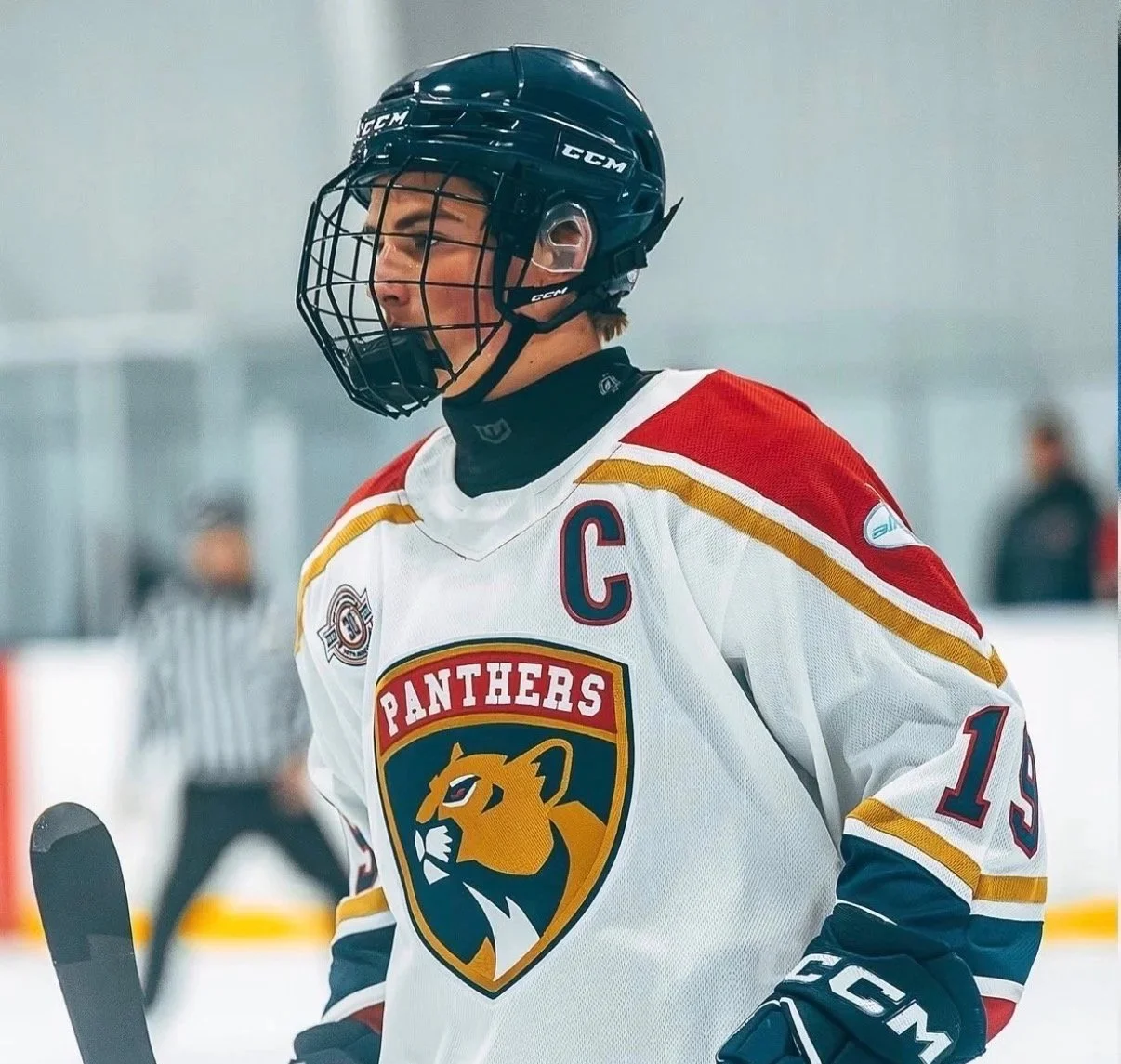 Hockey player in a white, red, and navy jersey with a panther logo, wearing a black helmet and gloves, on ice during a game.