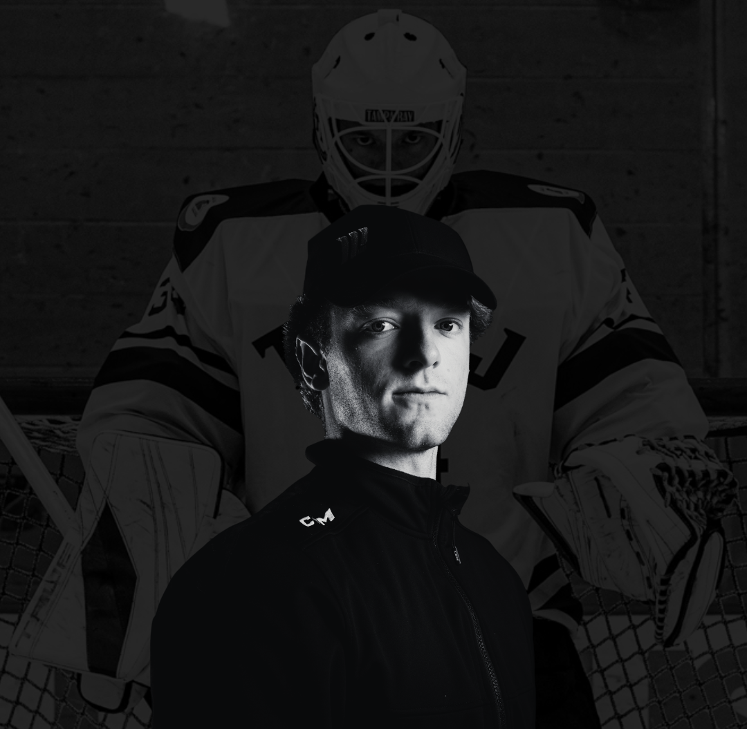 A young man wearing a black jacket and a cap, standing in front of a large black-and-white photo of a hockey goalie in full gear, including a mask, on an ice hockey rink.