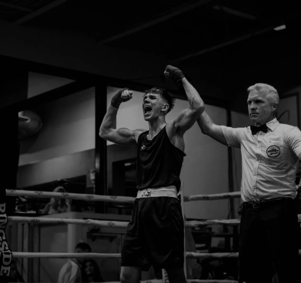 Boxer in boxing ring celebrating victory with arms raised, referee holding up his arm, black and white image.