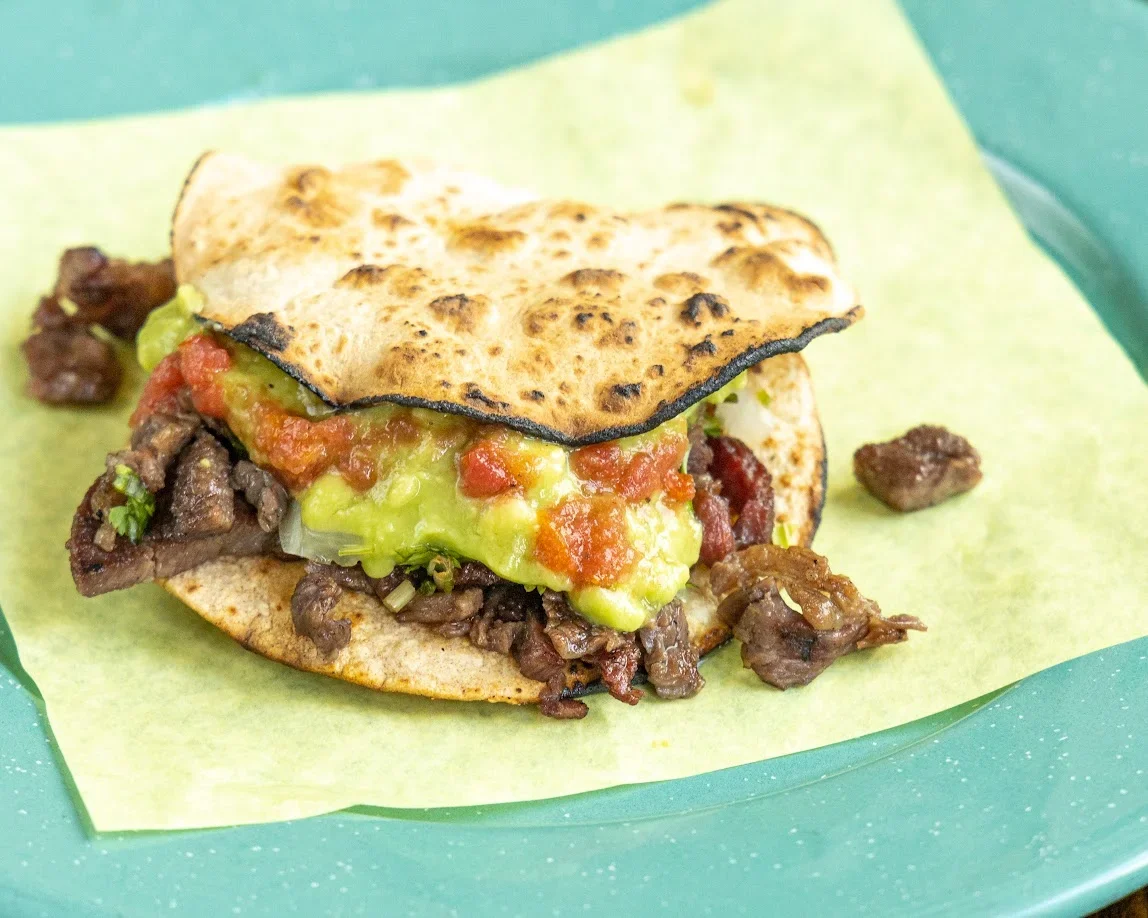 A taco filled with cooked beef, guacamole, and salsa on a grilled tortilla