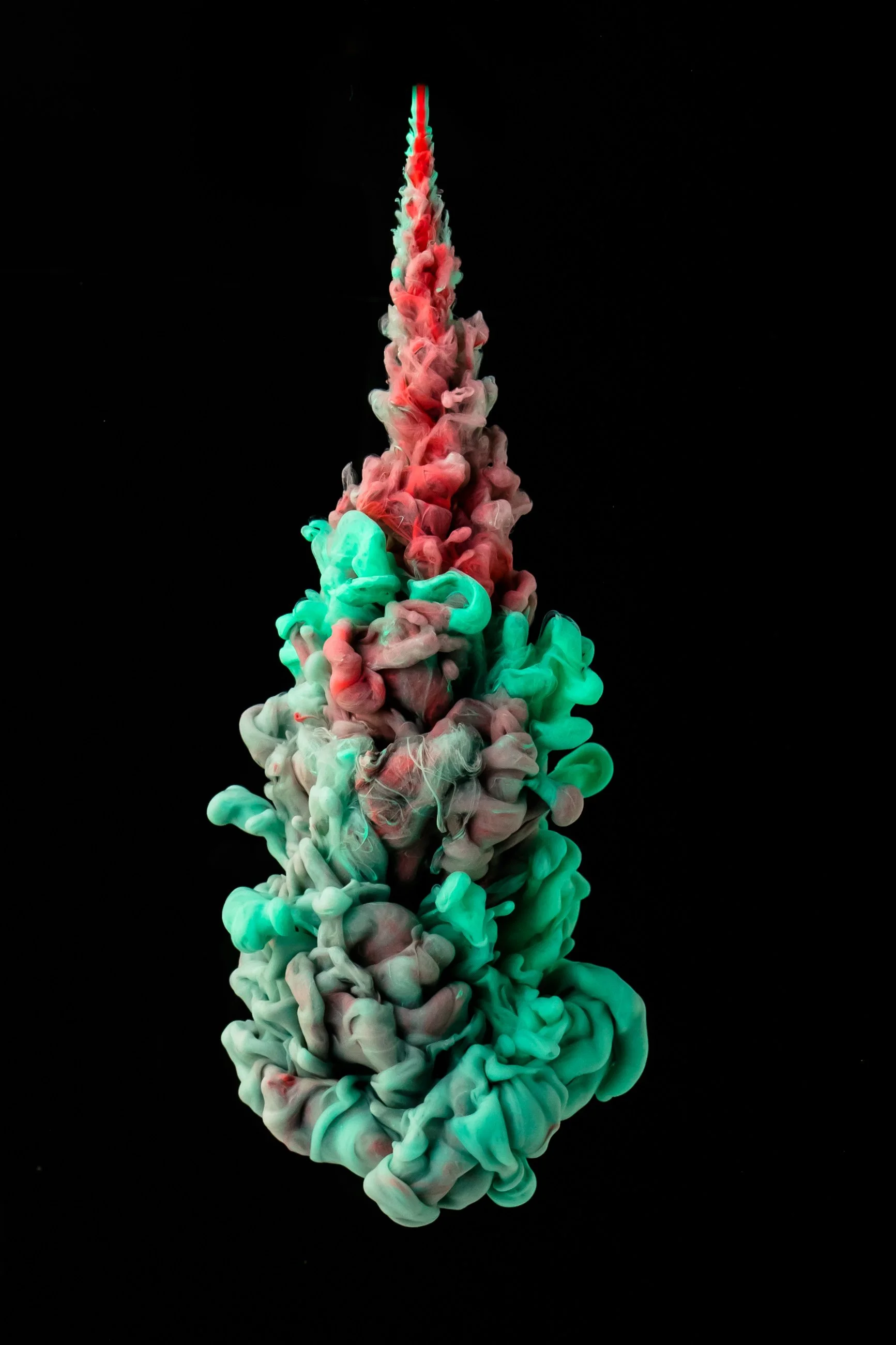 Colorful ink swirling in black water, forming fluffy cloud-like shapes in pink, green, and white hues.