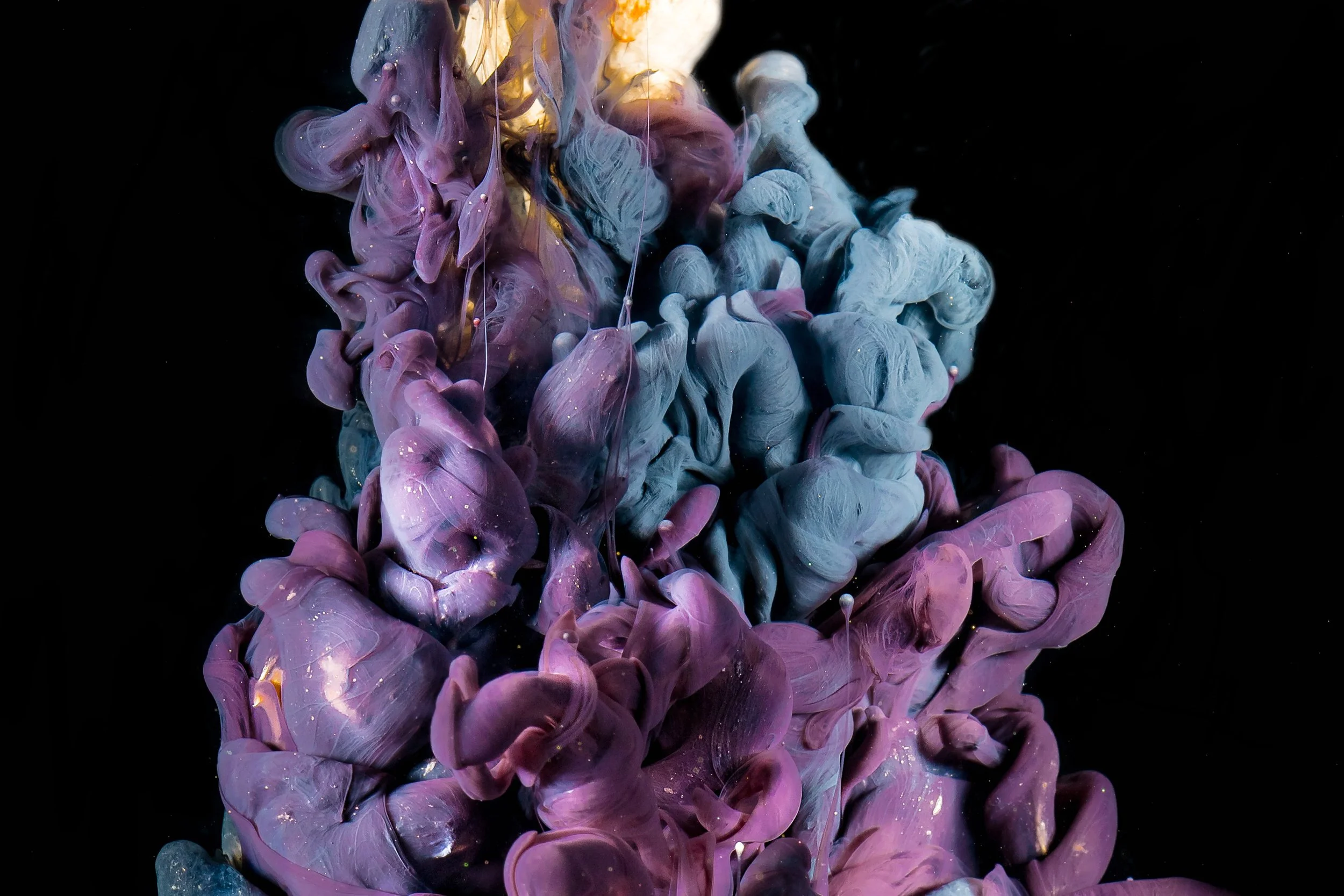 Swirling mixture of purple, pink, and blue ink in water against a black background.