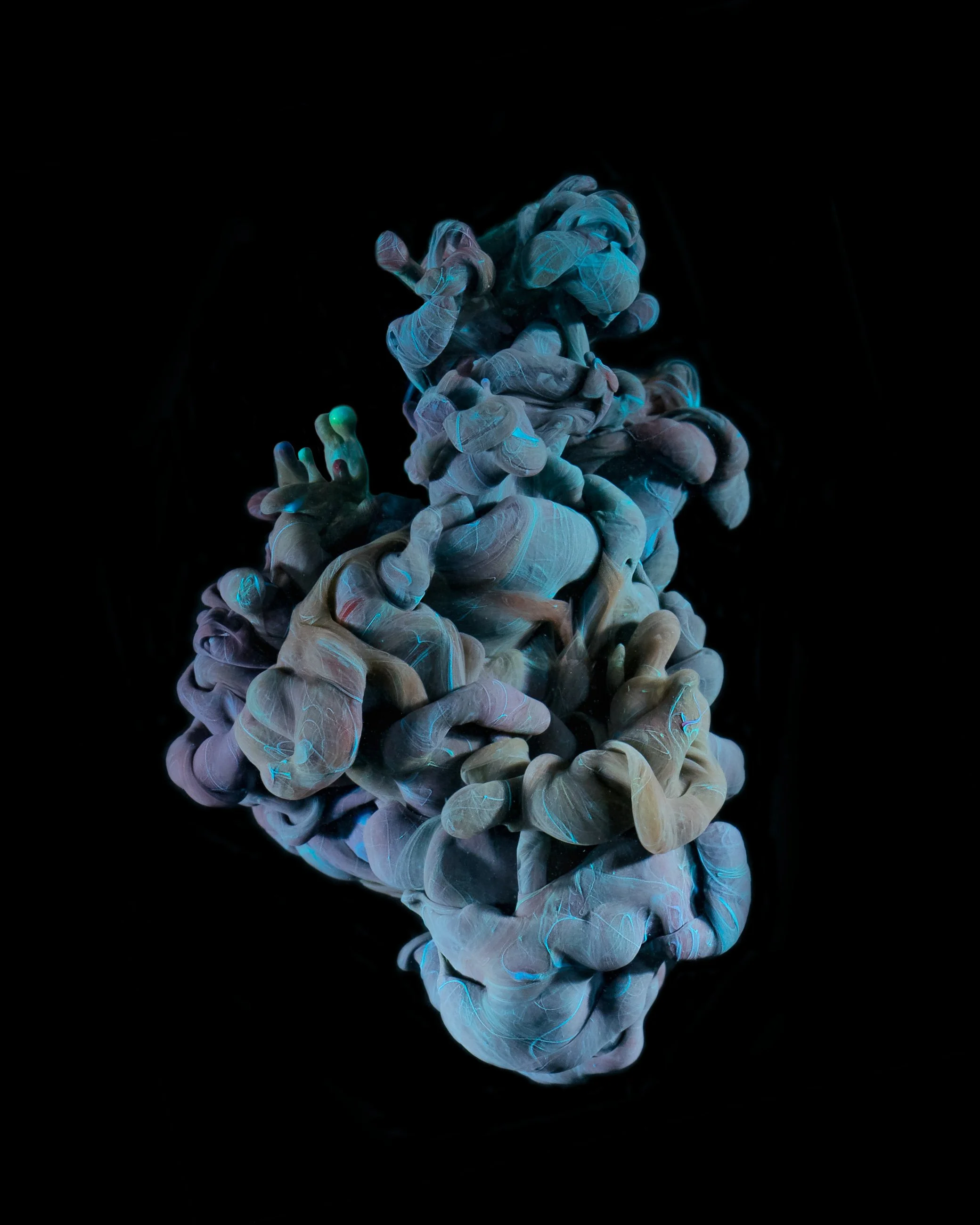 Colorful ink swirling in water against a black background, creating abstract, cloud-like formations.