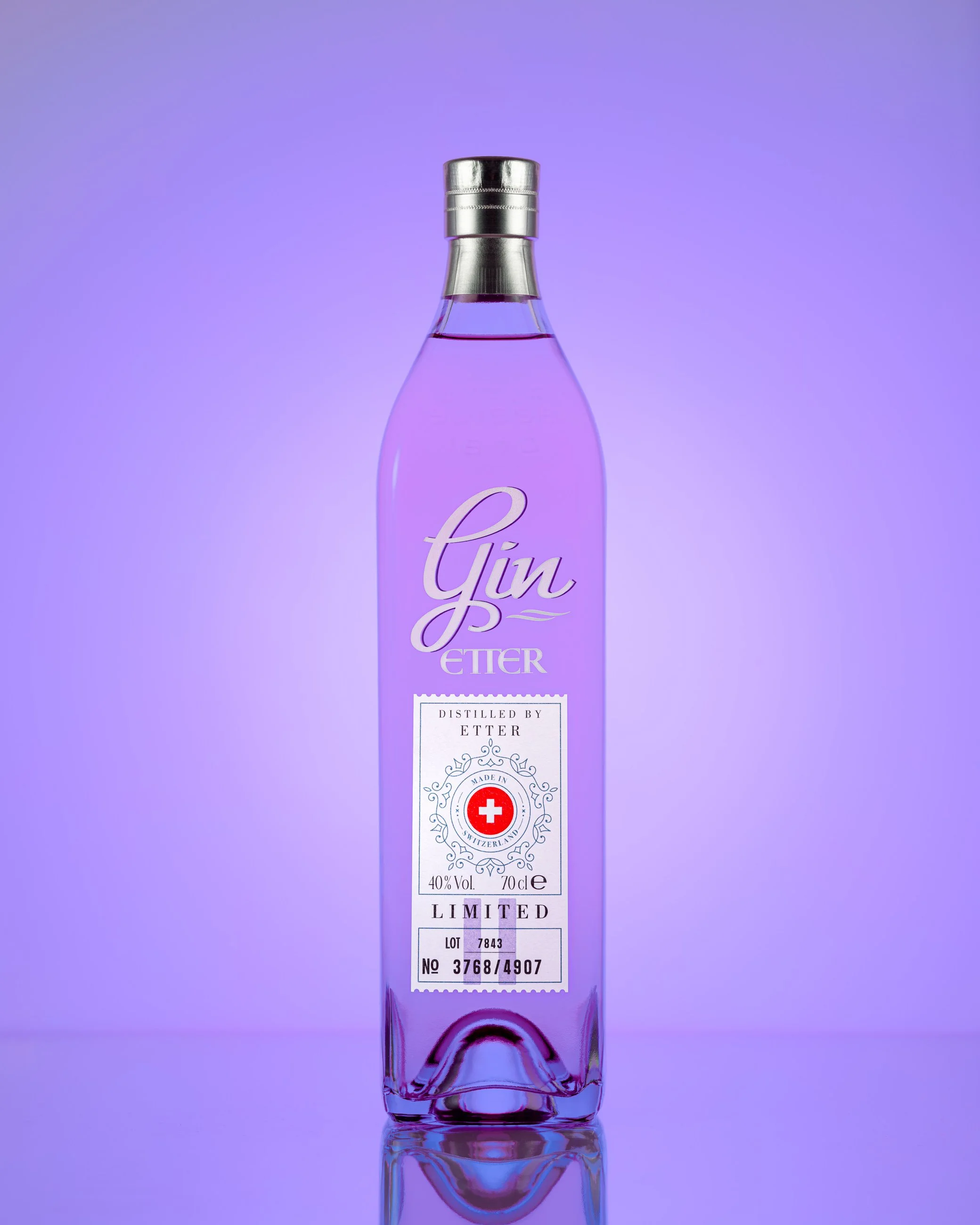 Purple gin in clear bottle photographed with purple gradient background in studio still life composition