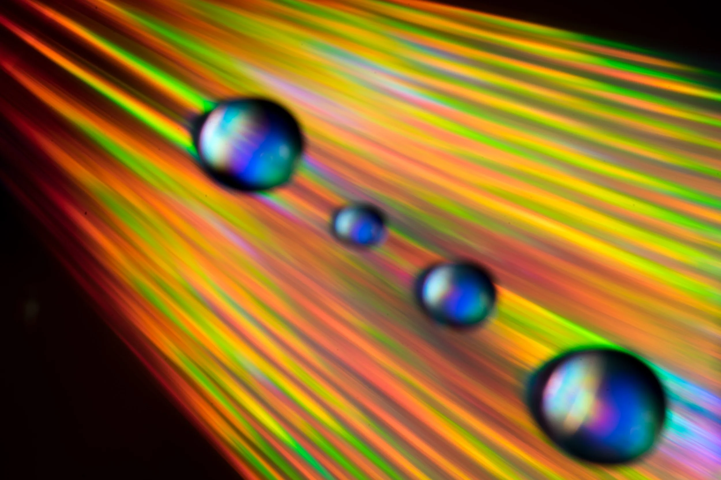 Close-up of colorful rainbow light reflections on a smooth surface with four water droplets.