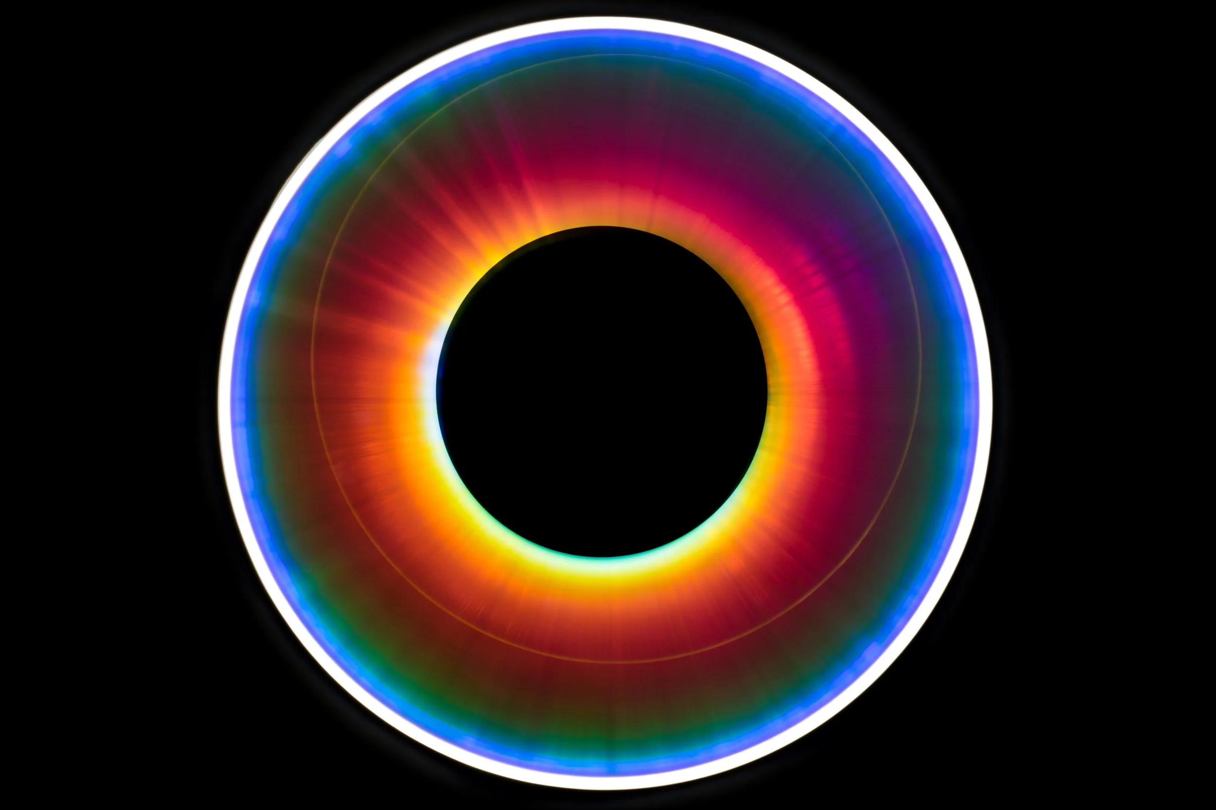 A colorful circular light ring with gradient hues of blue, purple, pink, orange, yellow, and green against a black background.