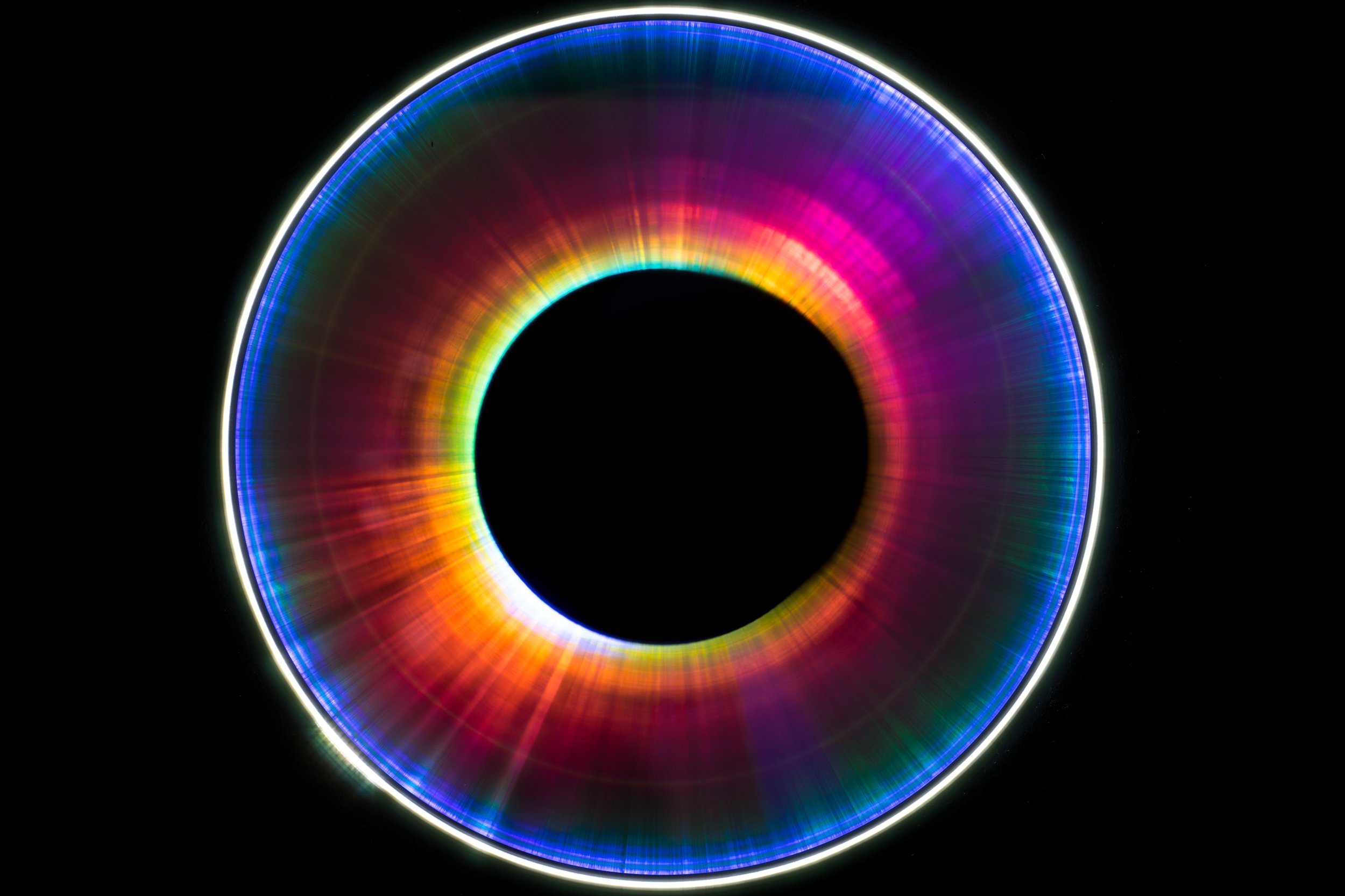 Colorful illuminated ring with rainbow gradient and a black center, against a black background.