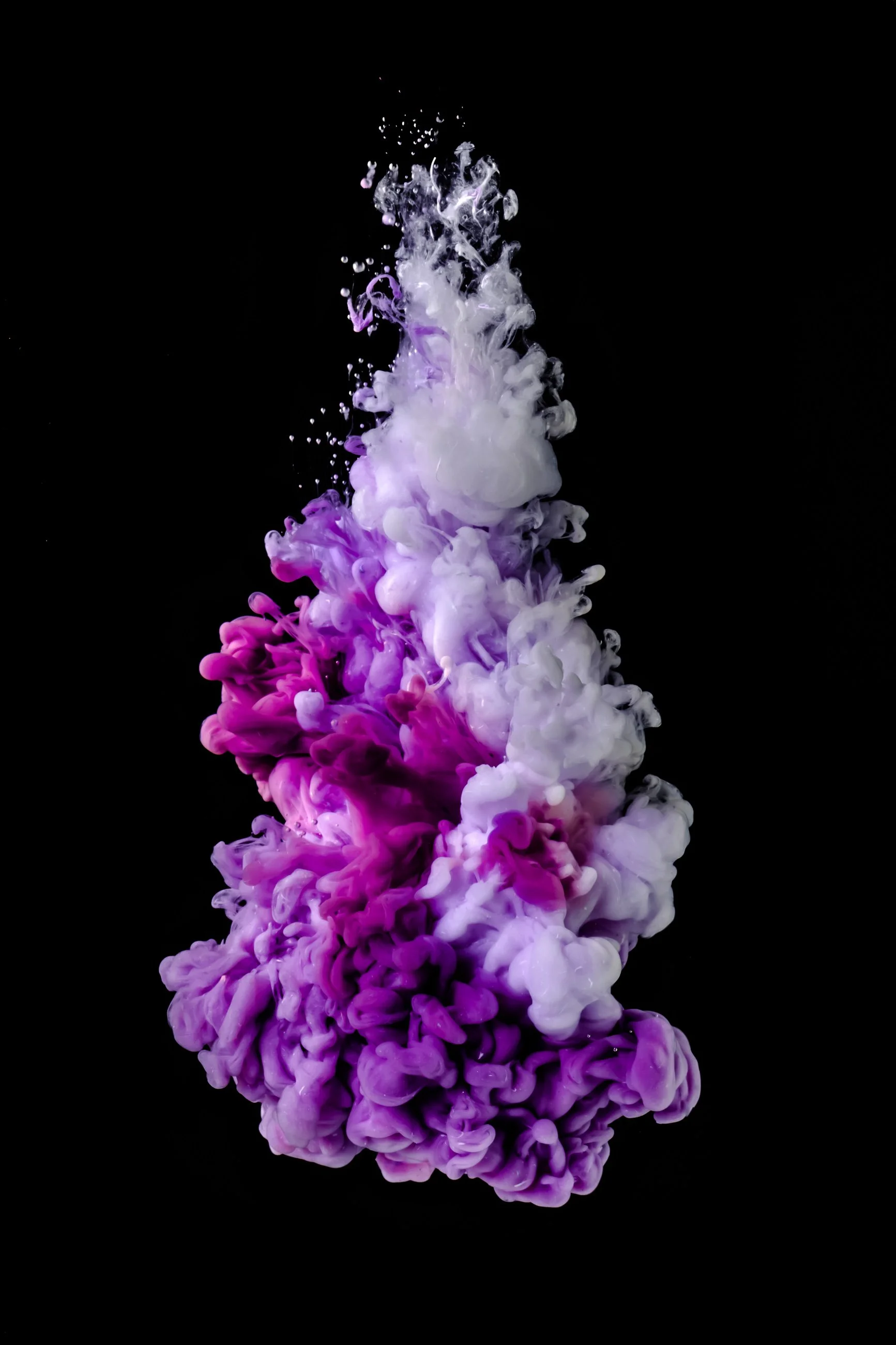 Colorful ink dispersing in water against a black background, creating purple, pink, and white cloud patterns.
