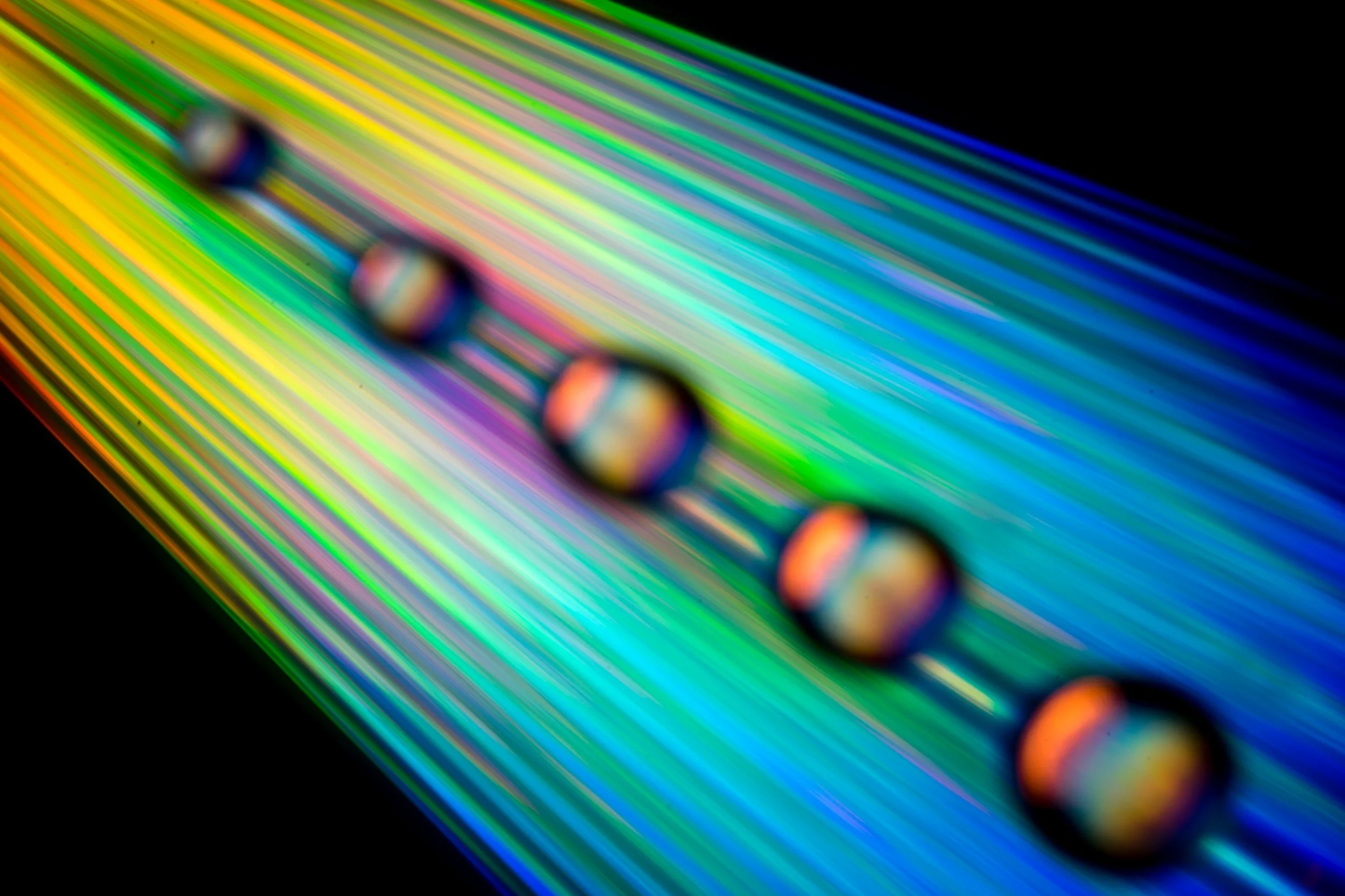 Close-up of a rainbow-colored surface with four droplets aligned in a row, reflecting the vibrant colors.