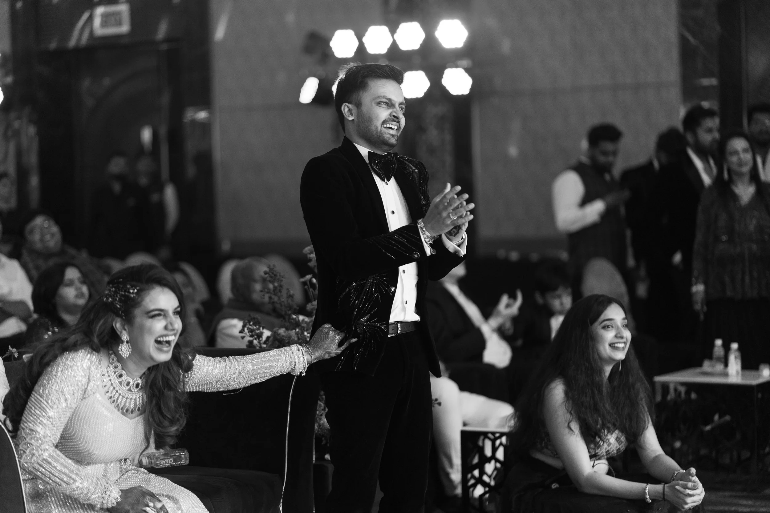 People attending a formal event or celebration, smiling and enjoying themselves, with some seated and some standing, in a decorated indoor venue.