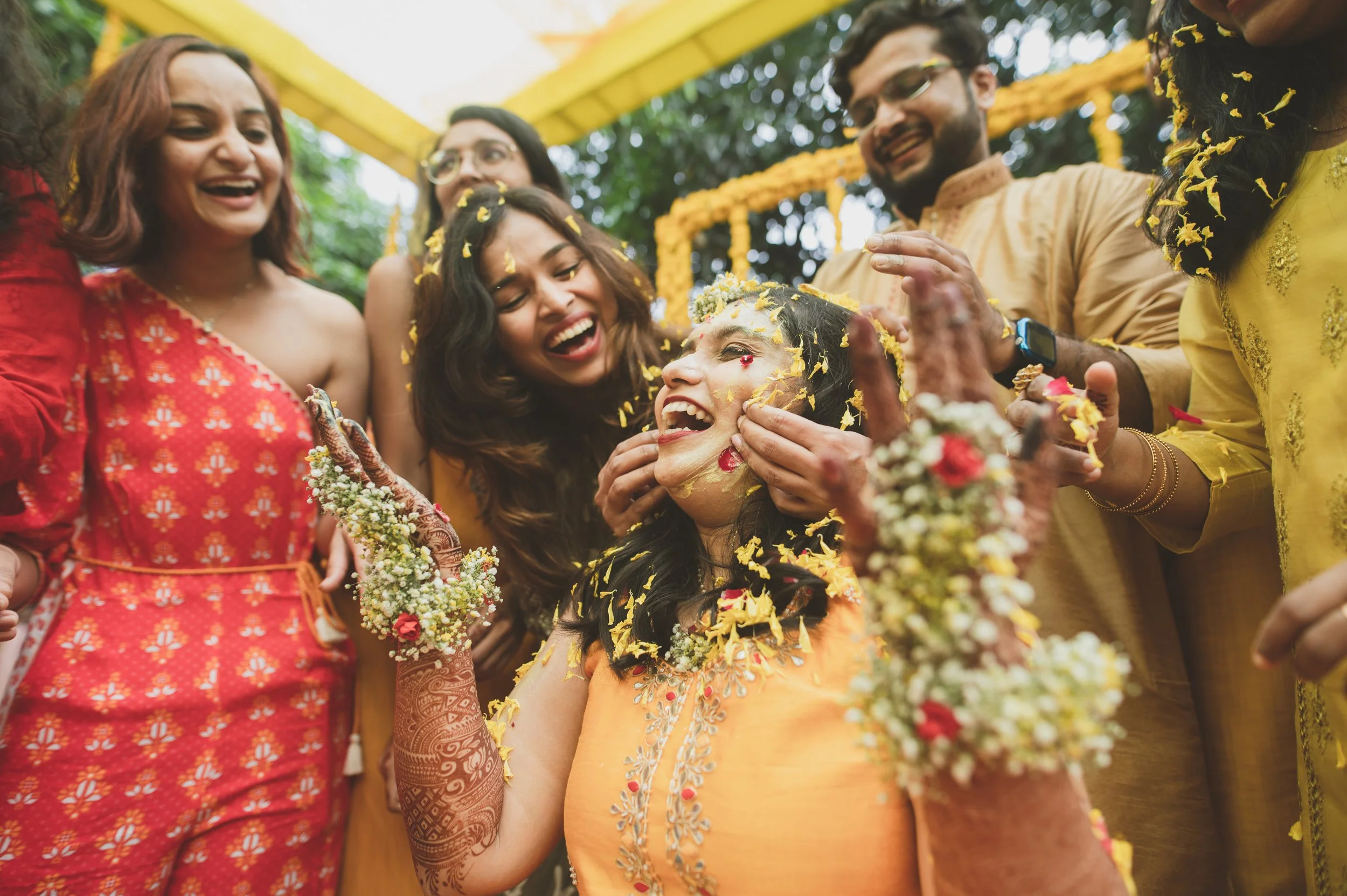 A woman celebrating her traditional Indian wedding ceremony with friends and family, with flower petals being showered on her.
