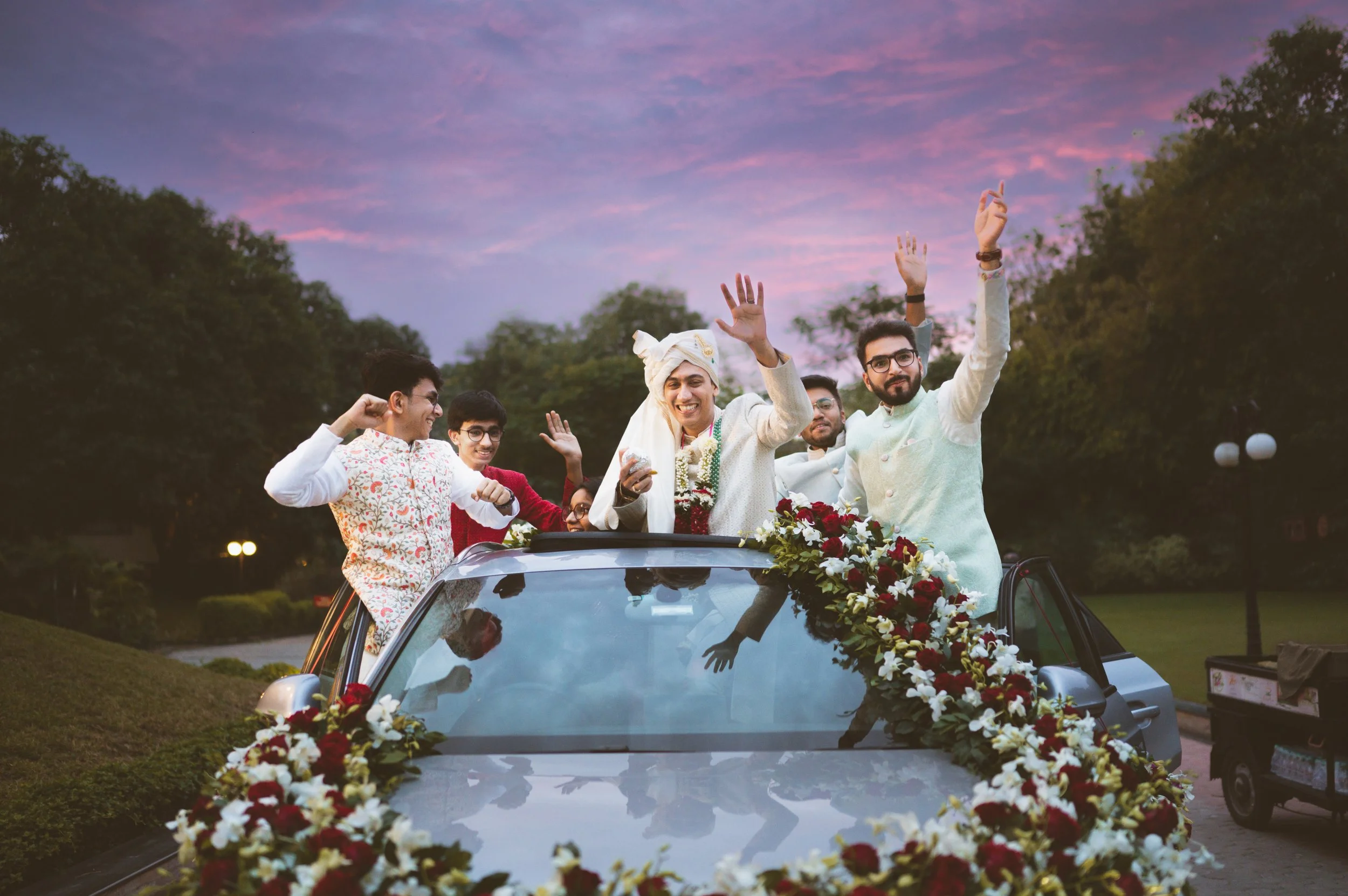 Group of men in traditional Indian attire celebrating on a decorated car at sunset.