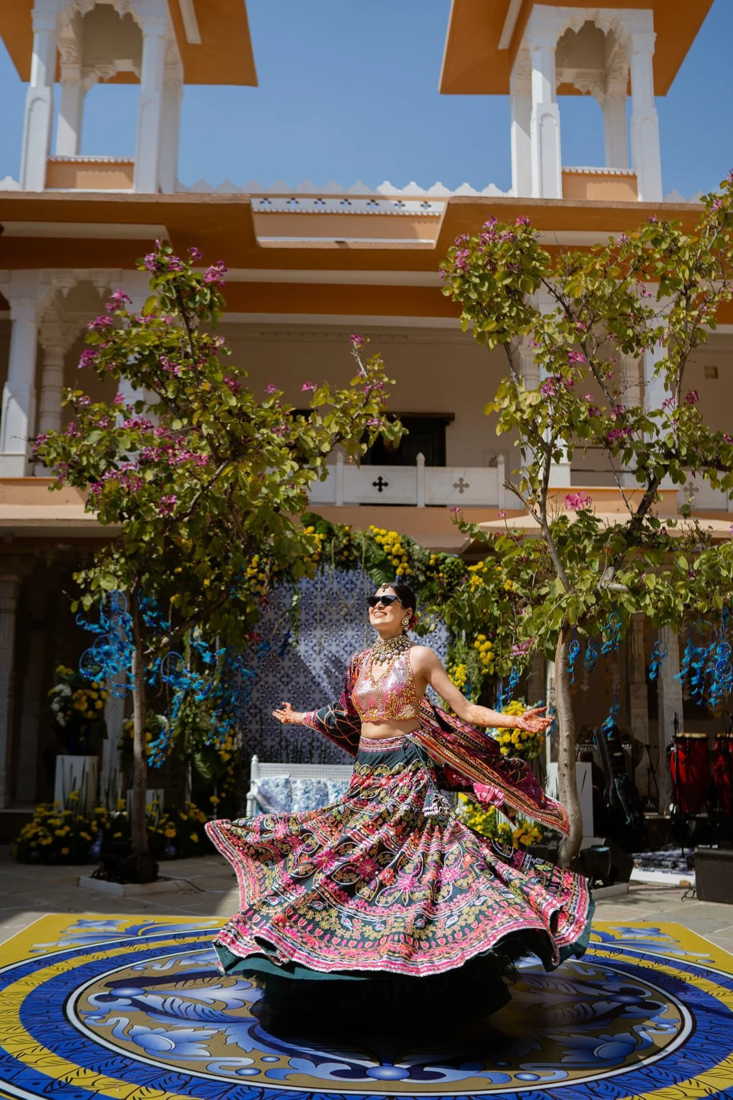 A woman in traditional attire dancing on a decorated outdoor stage with flowers and trees.