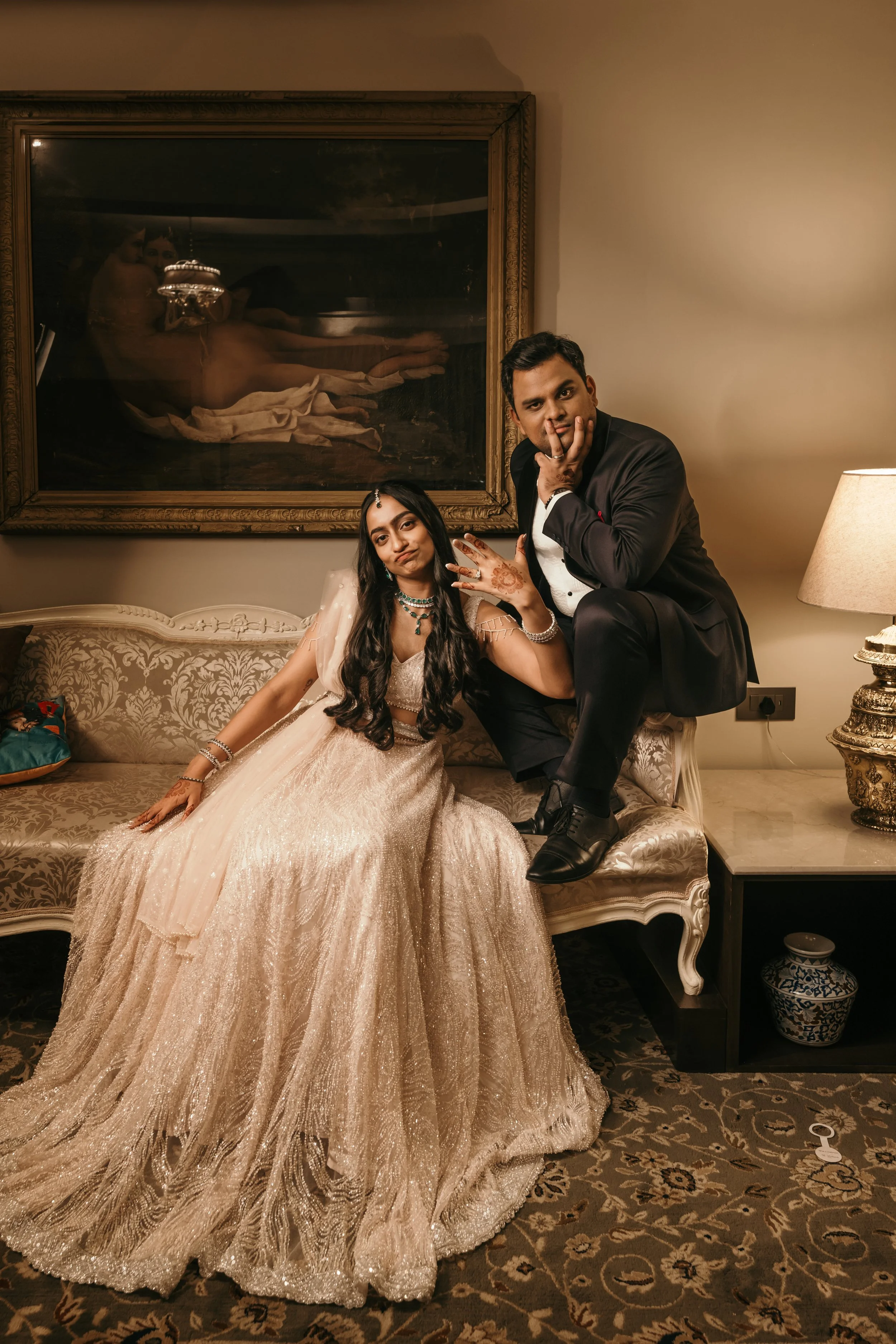 A couple dressed in formal attire posing inside a well-decorated room with a large mirror.