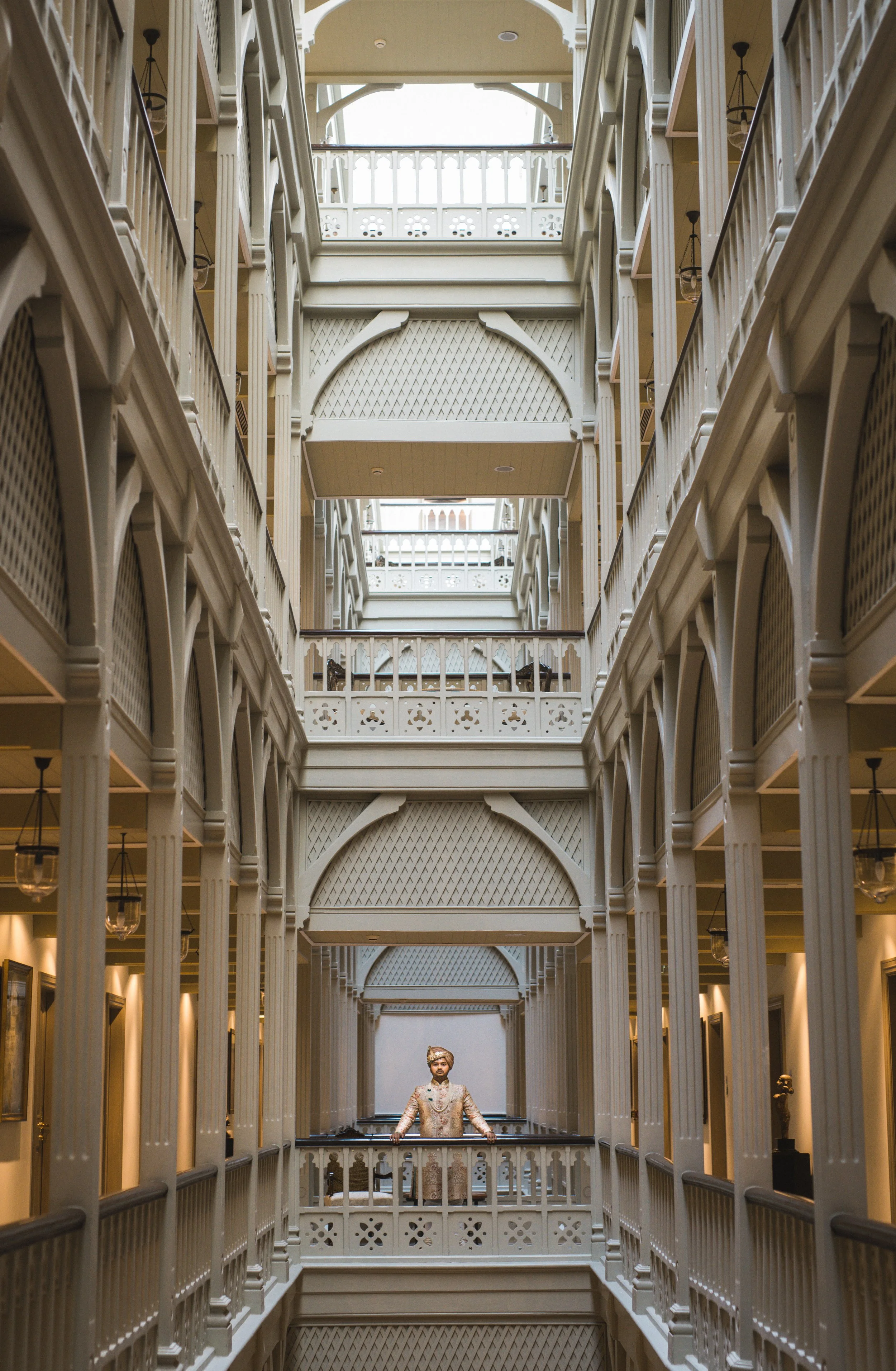 Interior view of a multi-story building with ornate white railings and arches, featuring a mannequin dressed in traditional clothing standing on a balcony.