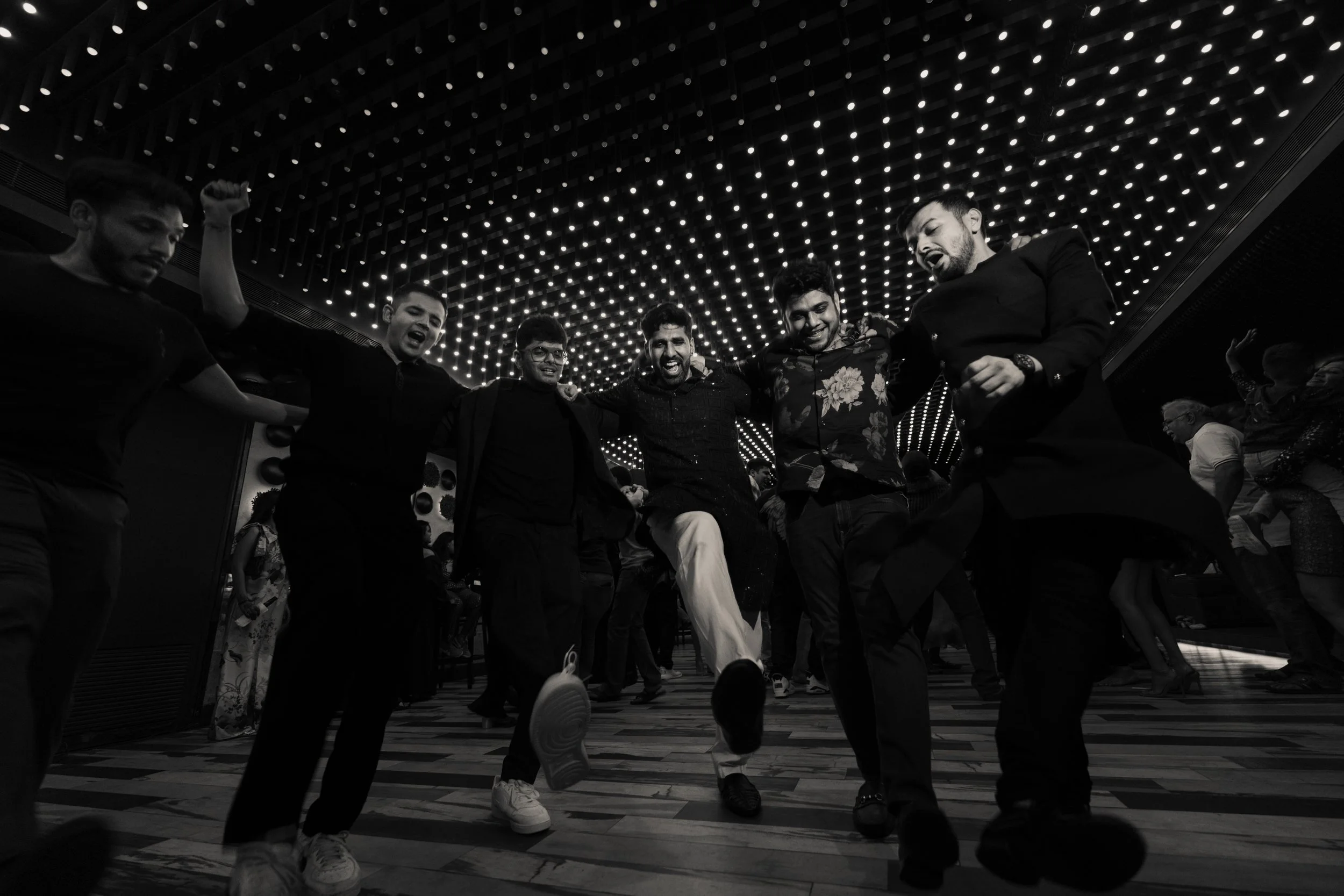 Group of friends dancing and enjoying themselves at a party under a ceiling decorated with string lights.